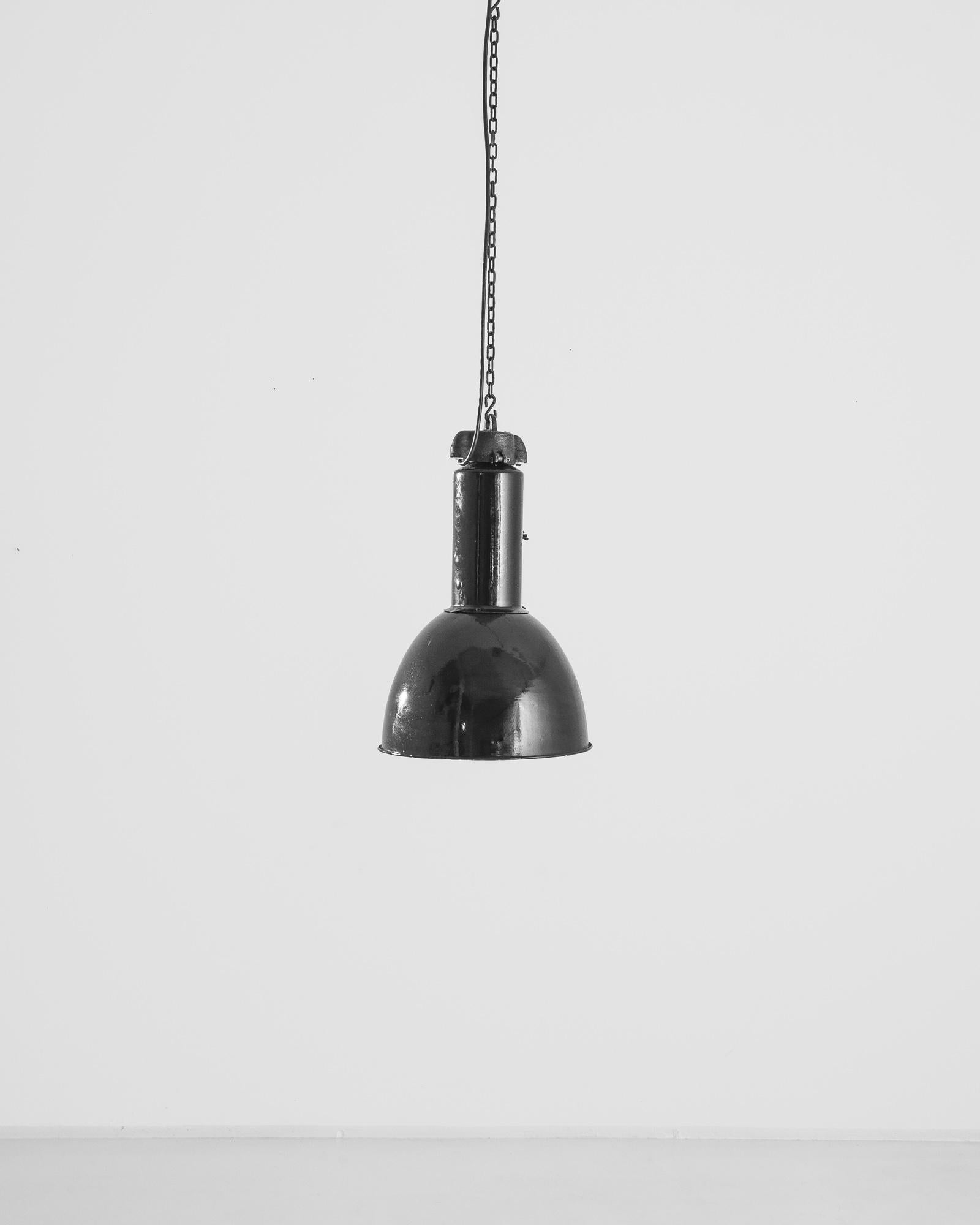 This 1930s Czech Industrial Pendant Lamp is an embodiment of raw, utilitarian design that has stood the test of time. Its enigmatic dark finish and robust metal construction speak of an era when products were made to last. The lamp features a