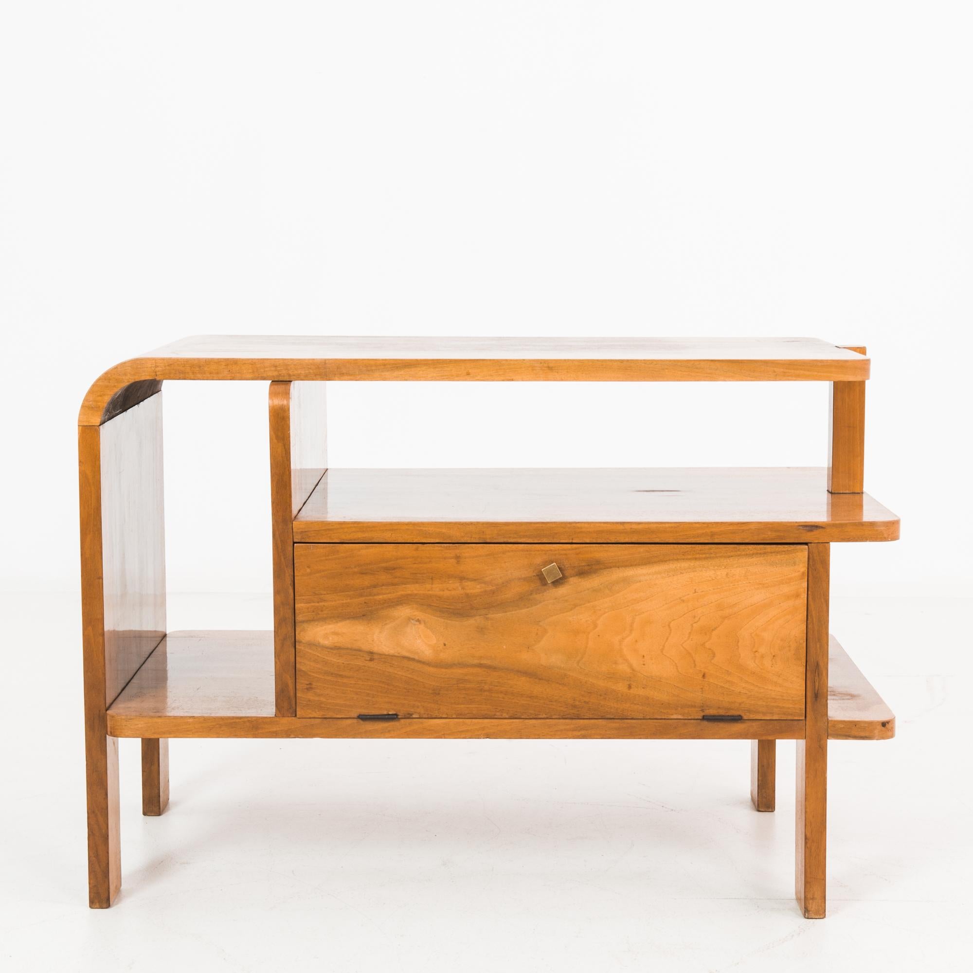 This wooden bedside table was made in the former Czechoslovakia, circa 1930. The table displays a versatility with the range of shelving space, including one with a hinged, drop-down door. Angular posts provide support, while rounded edges