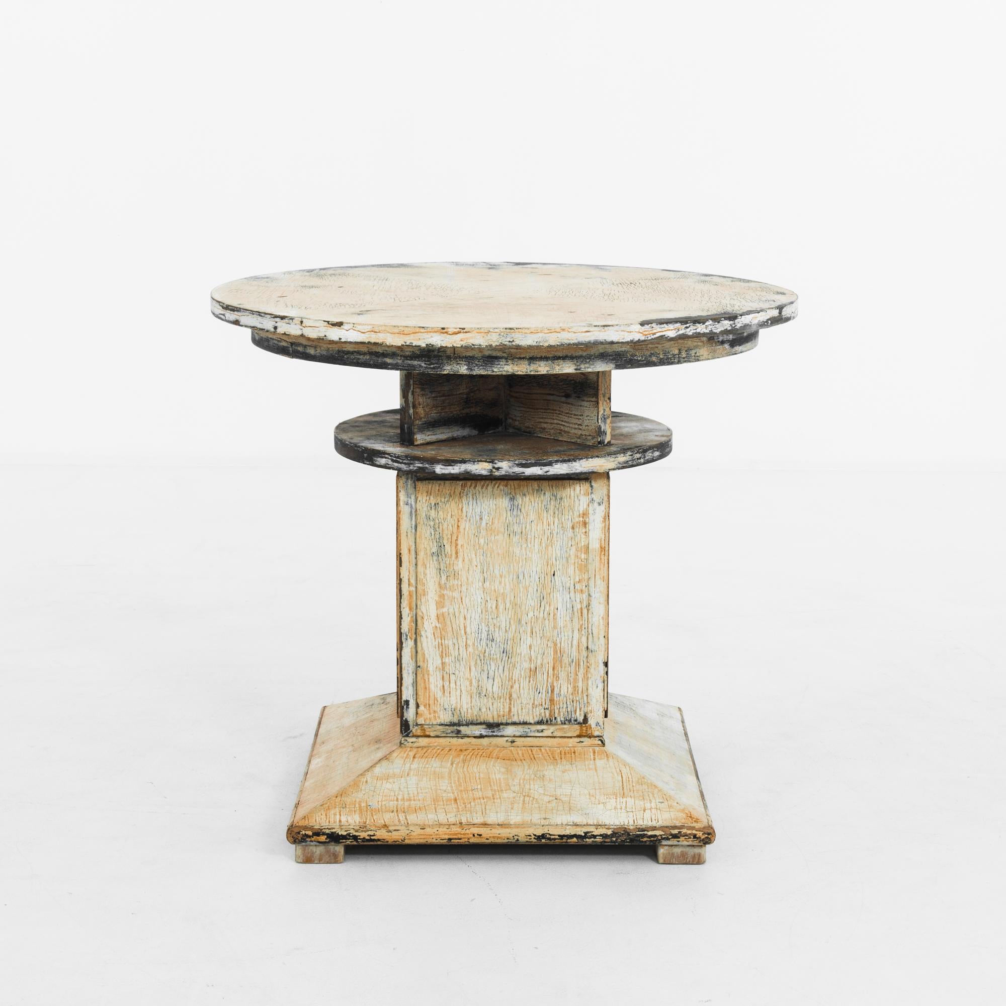 This wooden table was made in the former Czechoslovakia, circa 1930, and features a compelling combination of forms. An X-shaped apron connects the round tabletop and lower tier. The central rectangular post rests on a square base, which is gently