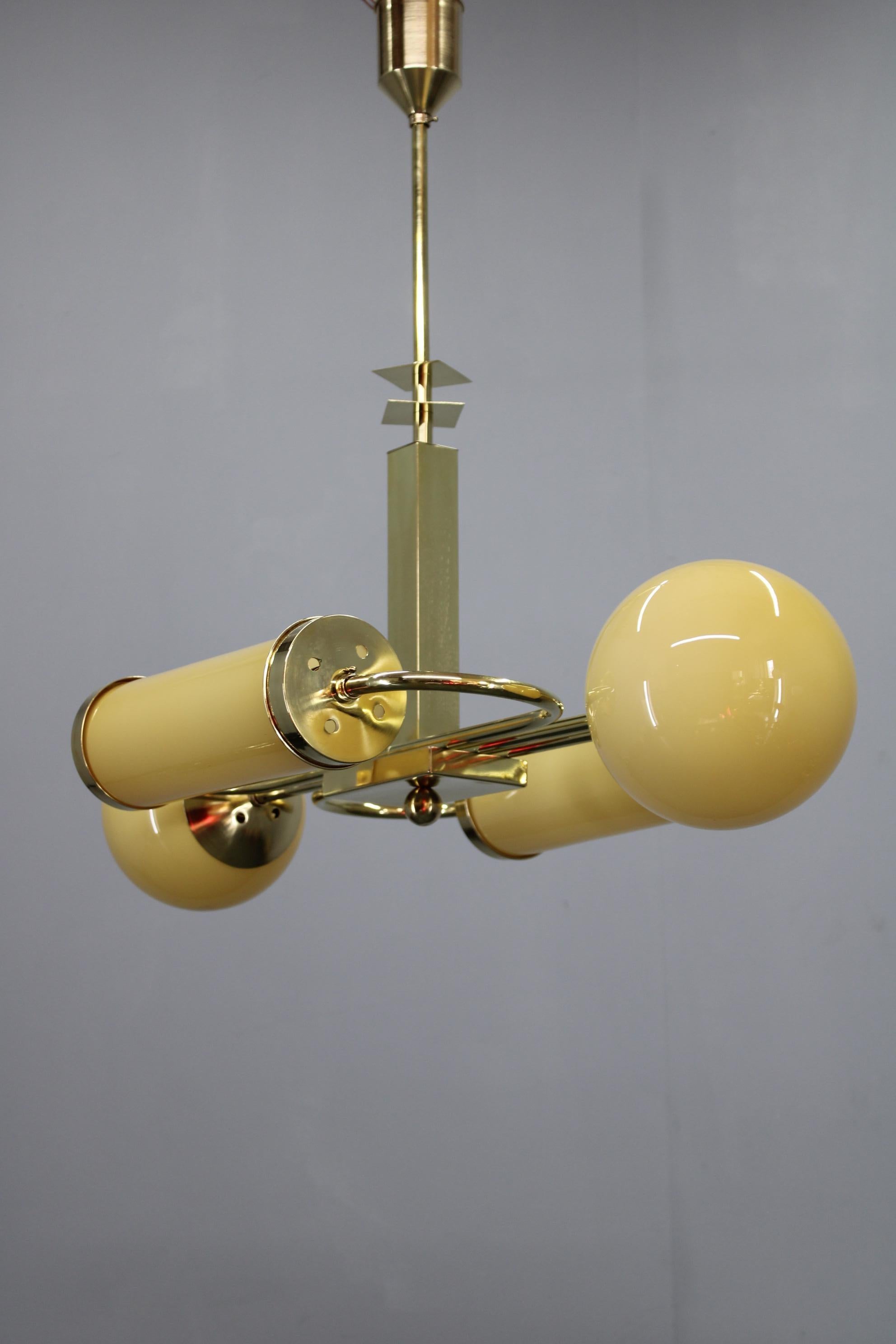 Exceptional Art Deco chandelier manufactured in Czechoslovakia in the 1930s, crafted in brass and fitted with two rounded opaline globe shades and two elongated opaline cylindrical glass shades. This rare mixed-form configuration embodies the