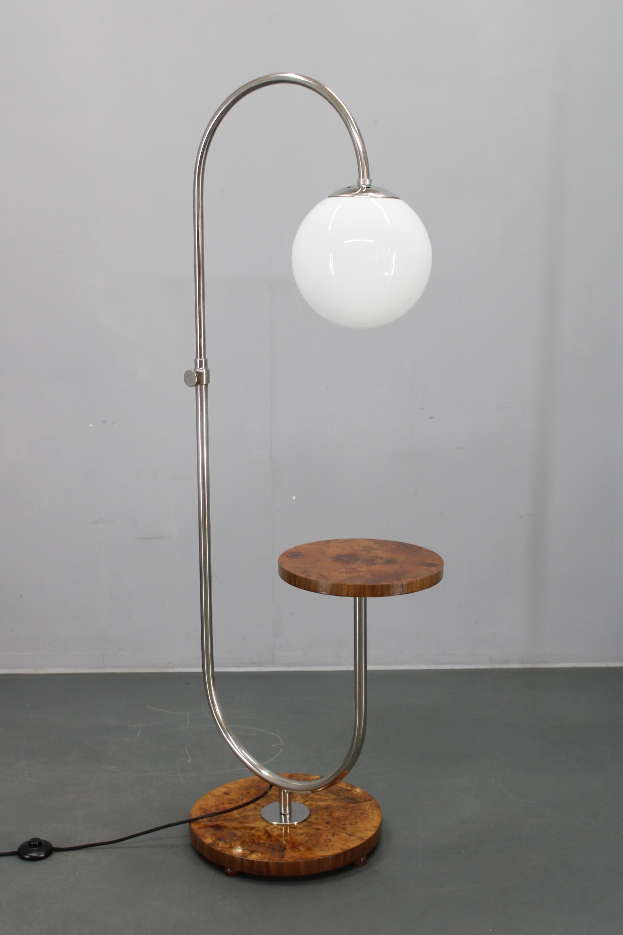 Elegante lámpara de pie Art Decó fabricada en Checoslovaquia en la década de 1930, que combina una refinada estructura de metal cromado con una esfera de cristal de leche soplado a mano y una base chapada en madera de nogal bellamente labrada y una