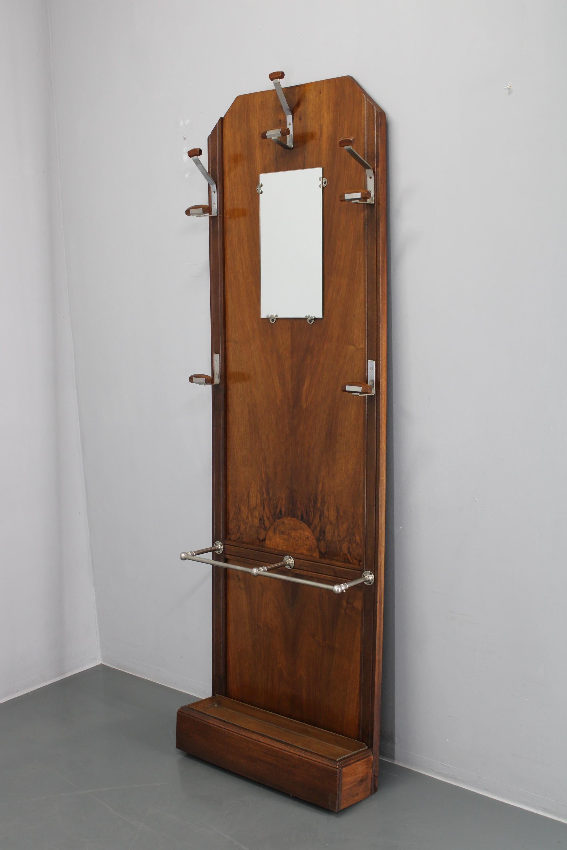 Elegant porte-manteau Art Deco fabriqué en CIRCA vers les années 1930, avec panneau en placage de noyer, crochets en métal nickelé et miroir central, ainsi qu'un porte-parapluie très pratique. En partie rénovée et bien conservée, cette tribune