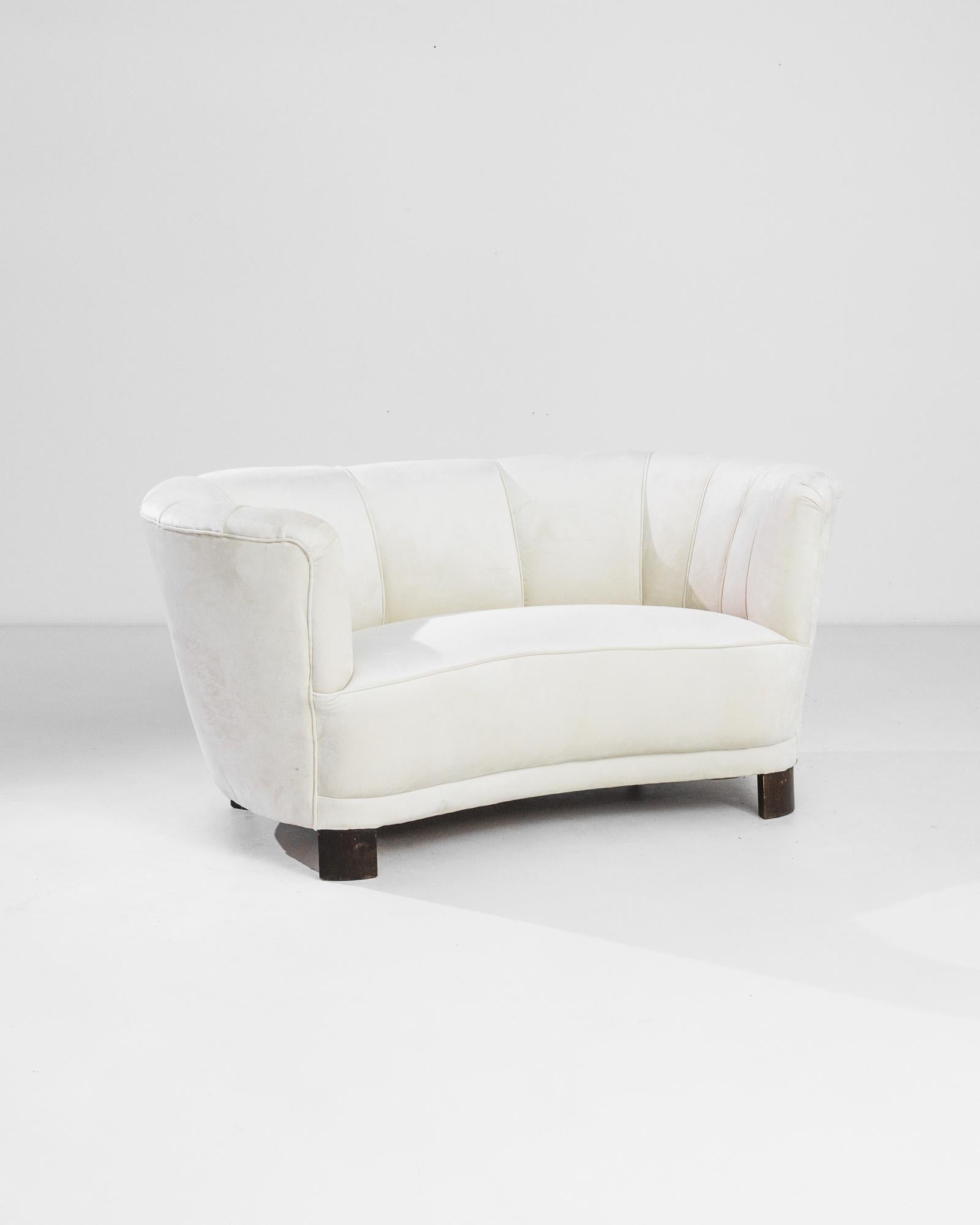 This curved sofa was produced in Denmark, circa 1930. With a solid wooden frame and refined curves, this harmoniously shaped sofa imparts a luxurious elegance. Fully upholstered with a cream fabric, its suede texture calls for a comfortable stay-in