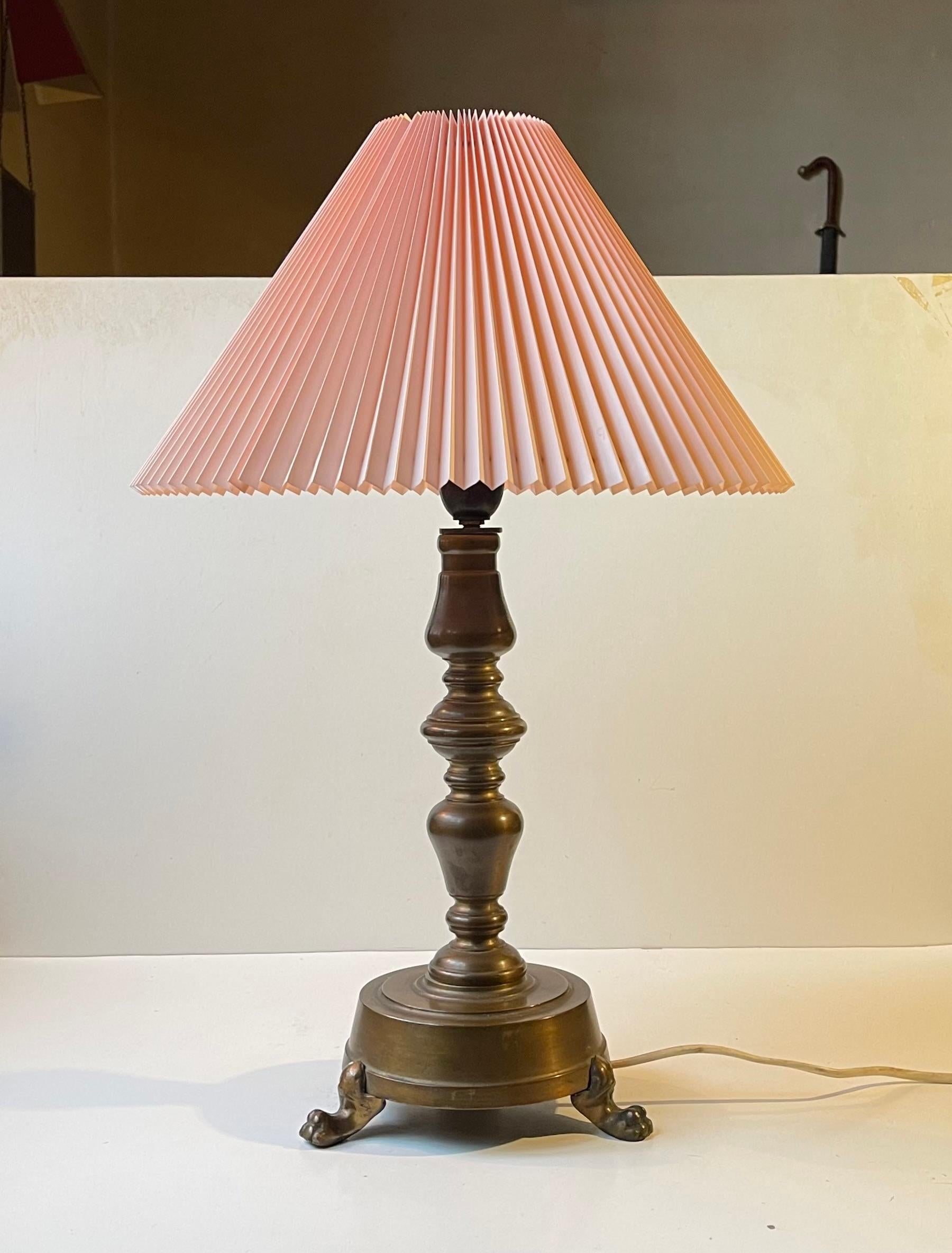 A stylish column table lamp with lion paws - feet executed in patinated bronze and featuring a fluted vintage pink shade. It was made during the 1930s by a Danish metalworker and it still has its original bakelite socket with on/off switch.