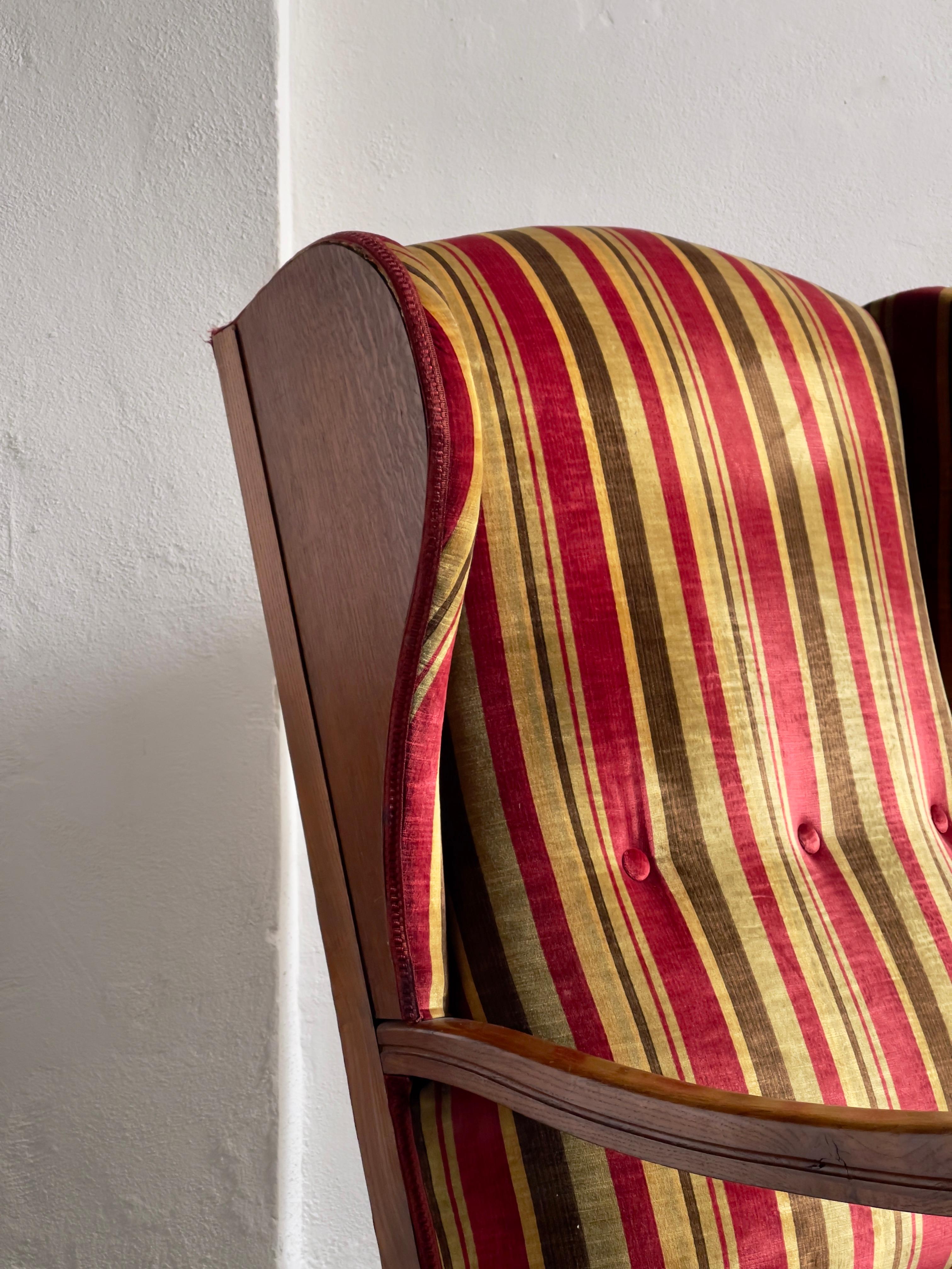 Fauteuil de salon ou fauteuil à oreilles en chêne massif fabriqué par un ébéniste danois dans les années 1930 et recouvert du plus beau et rare velours de coton pur de première qualité avec d'élégantes rayures rouges, vertes d'olive et dorées. Ce