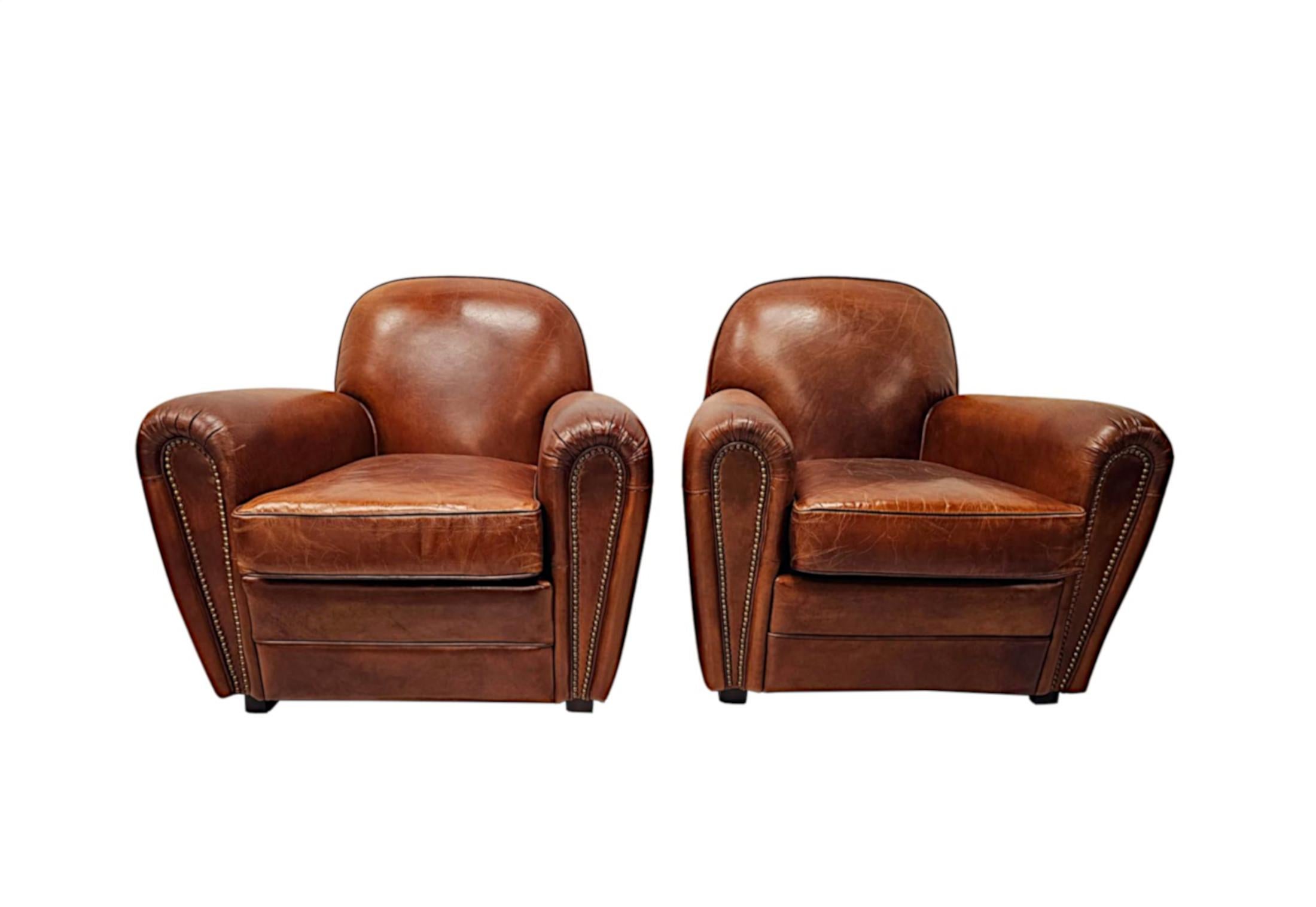 Un fabuloso sillón club de diseño de los años 30, de calidad excepcional y tapizado en cuero marrón de gran riqueza y elegancia, con un precioso acabado envejecido, tachuelas decorativas de latón y detalles de ribetes por toda la superficie.  El