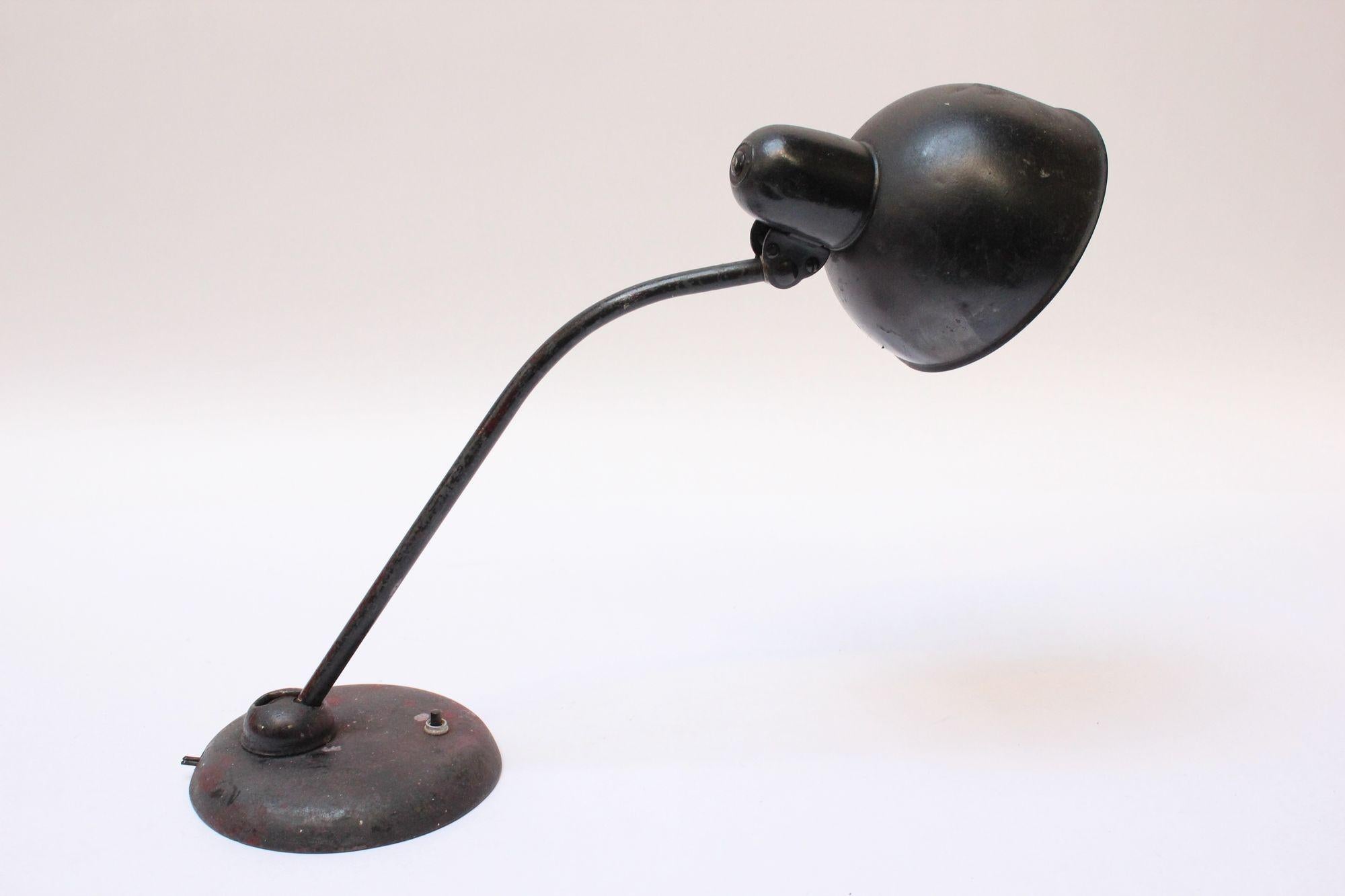 Desk/table lamp featuring an enameled metal shade and painted round metal base, circa 1930s. 
Features an adjustable shade and stem.
Naturally distressed condition showing paint marks, dents, and scratches. Visibly repainted at one point. Remains a
