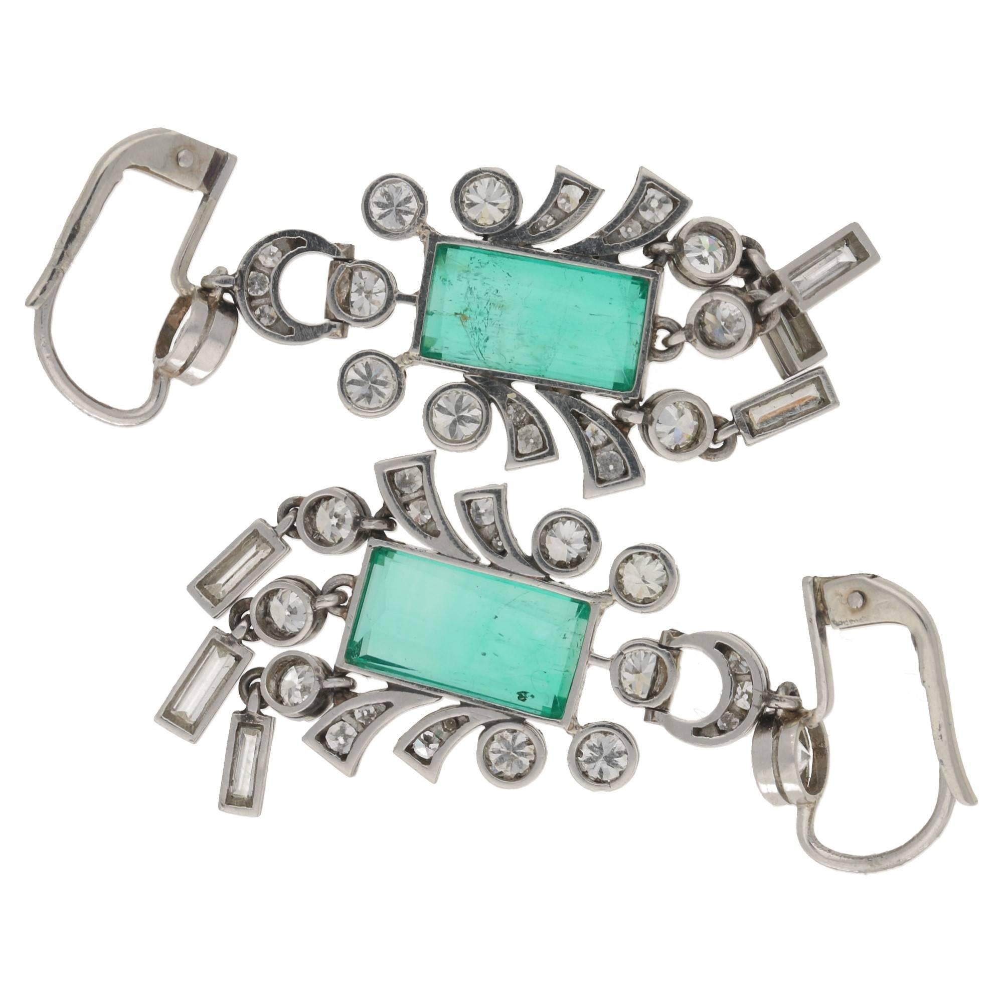 A beautiful pair of 1930's emerald and diamond earrings, The emerald cut emeralds are rub over set to the centre and framed by mixture of cuts, European cuts and baguette cuts. The earrings are affixed to period clips and are set fully in