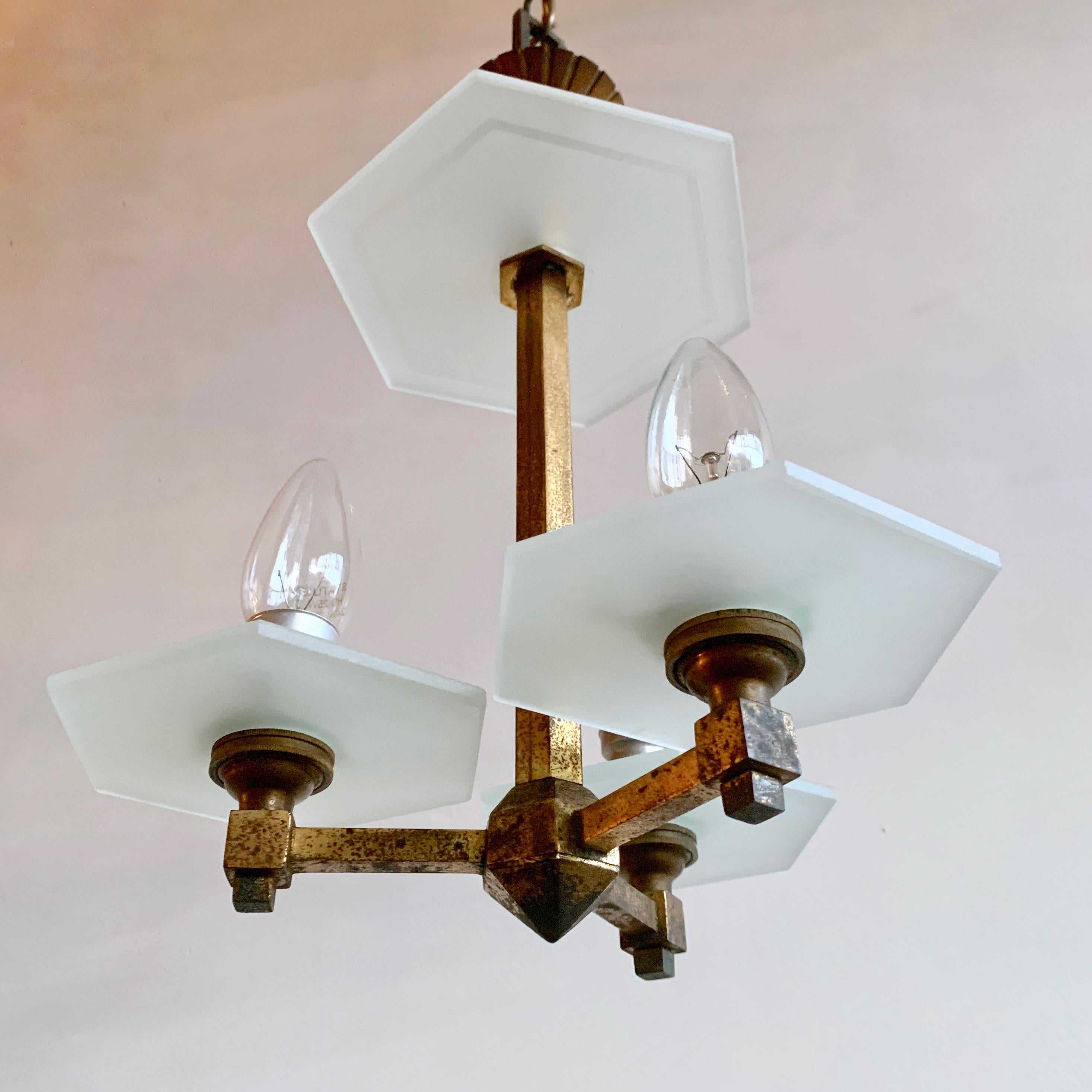 Petite 1930s Art Deco brass chandelier with hexagonal frosted glass pieces. This chandelier has three lamps. This piece was originally gilt that has aged leaving an off-black and gold patina. It has elegant proportions and would suit a hall way or