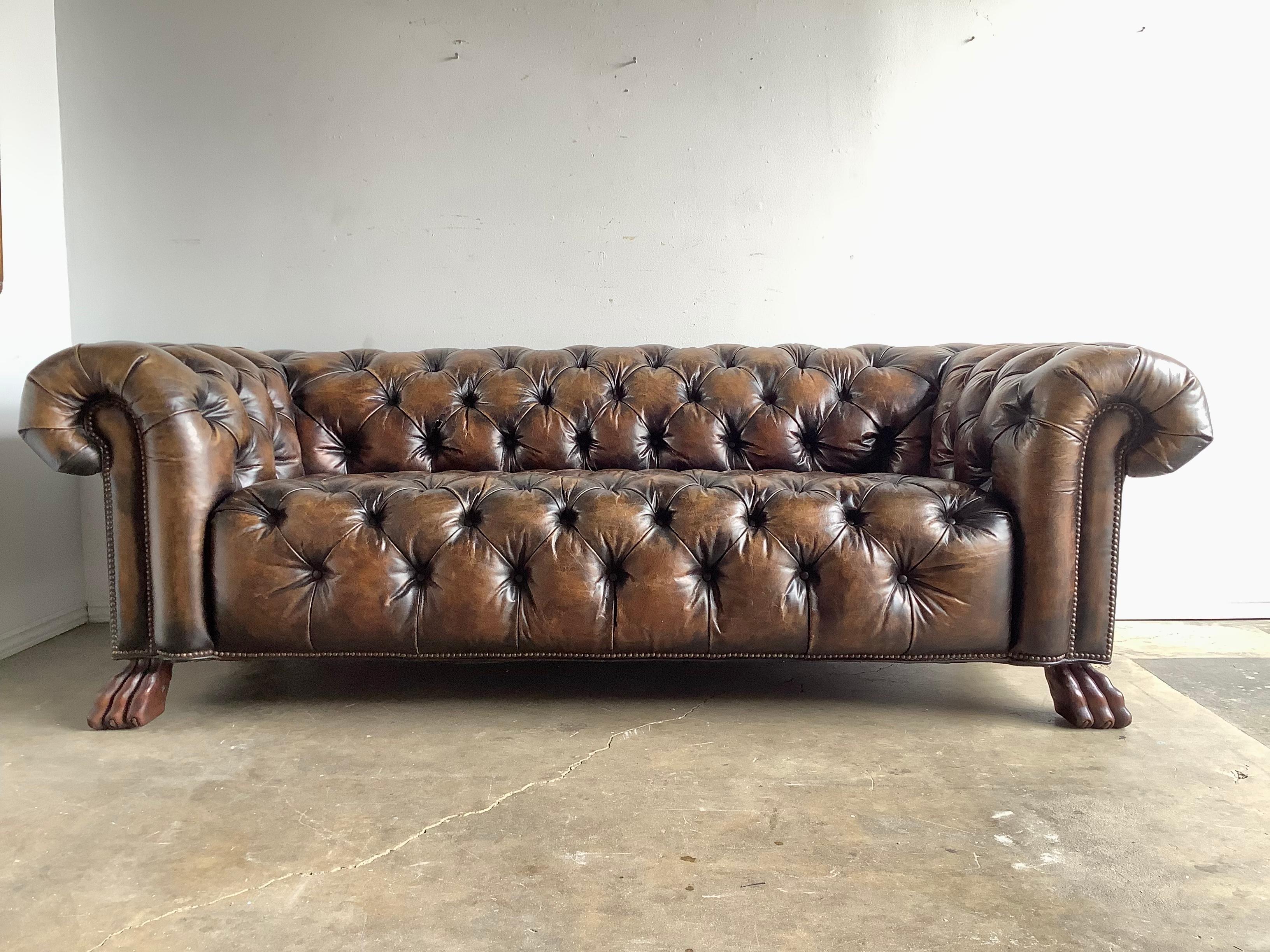 English leather tufted tobacco colored Chesterfield style sofa with nailhead trim detail. The sofa stands on four hand carved wood lion paw feet