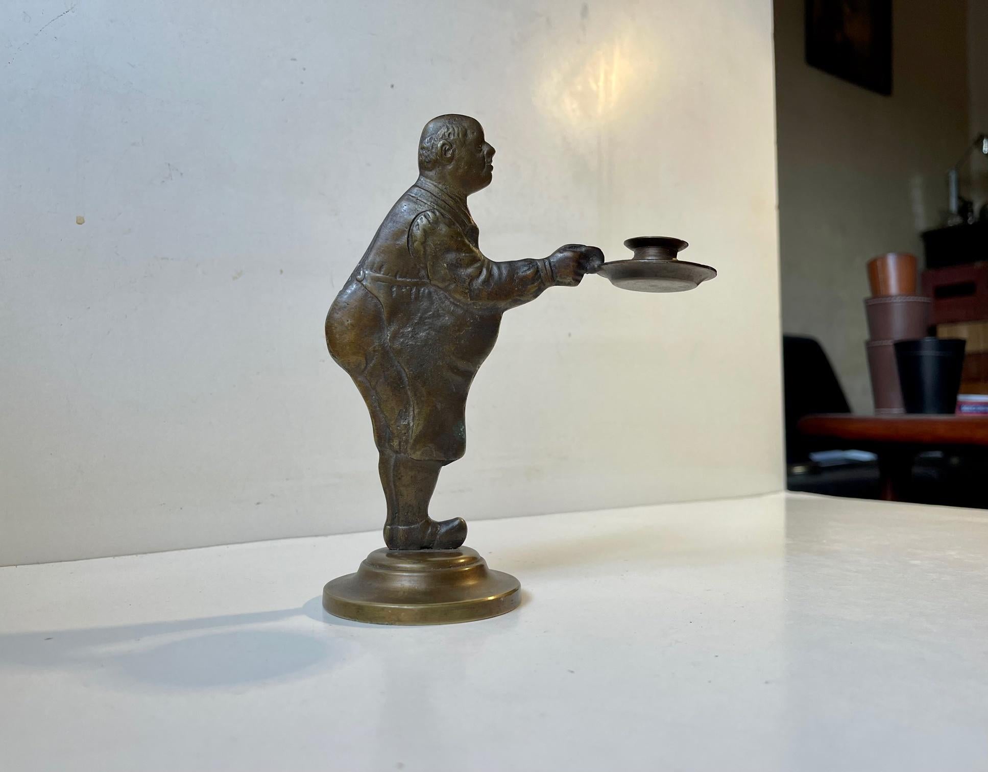 Humorous Storm P. (Danish cartoonist7/illustrator) inspired candlestick in patinated bronze. Motif: corpulent man/Blacksmith Details/attributed to both sides. It is to be installed with a taper/1 cm candle. Measurements: H: 18 cm, W: 15 cm.
