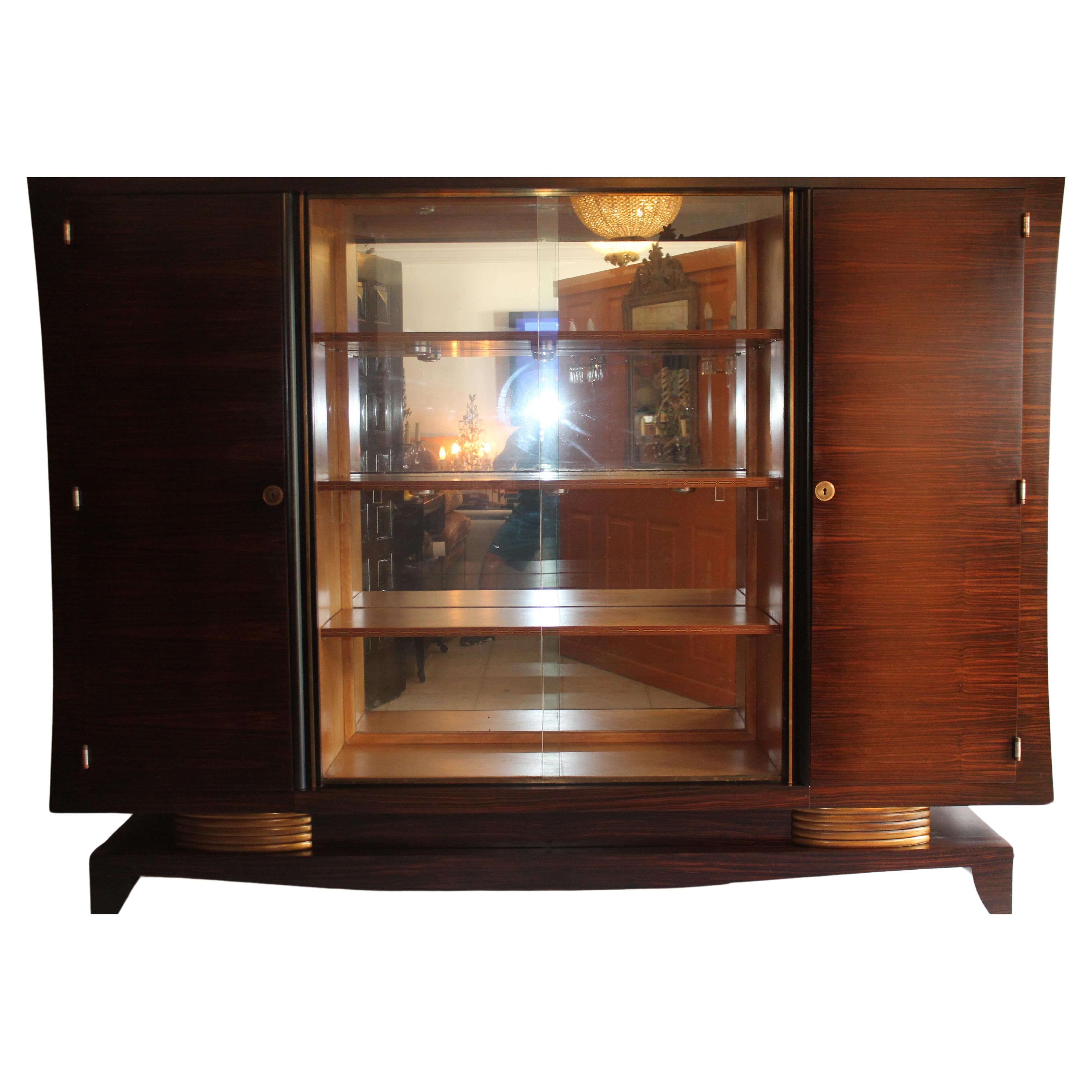 On Offer is a Grand Scale Macassar Ebony 3- Part Cabinet attributed Jules Leleu. All original, left cabinet door opens to reveal a finished Secretary. In the center of the cabinet is a shelved and mirrored Vitrine -display case with glass doors. On