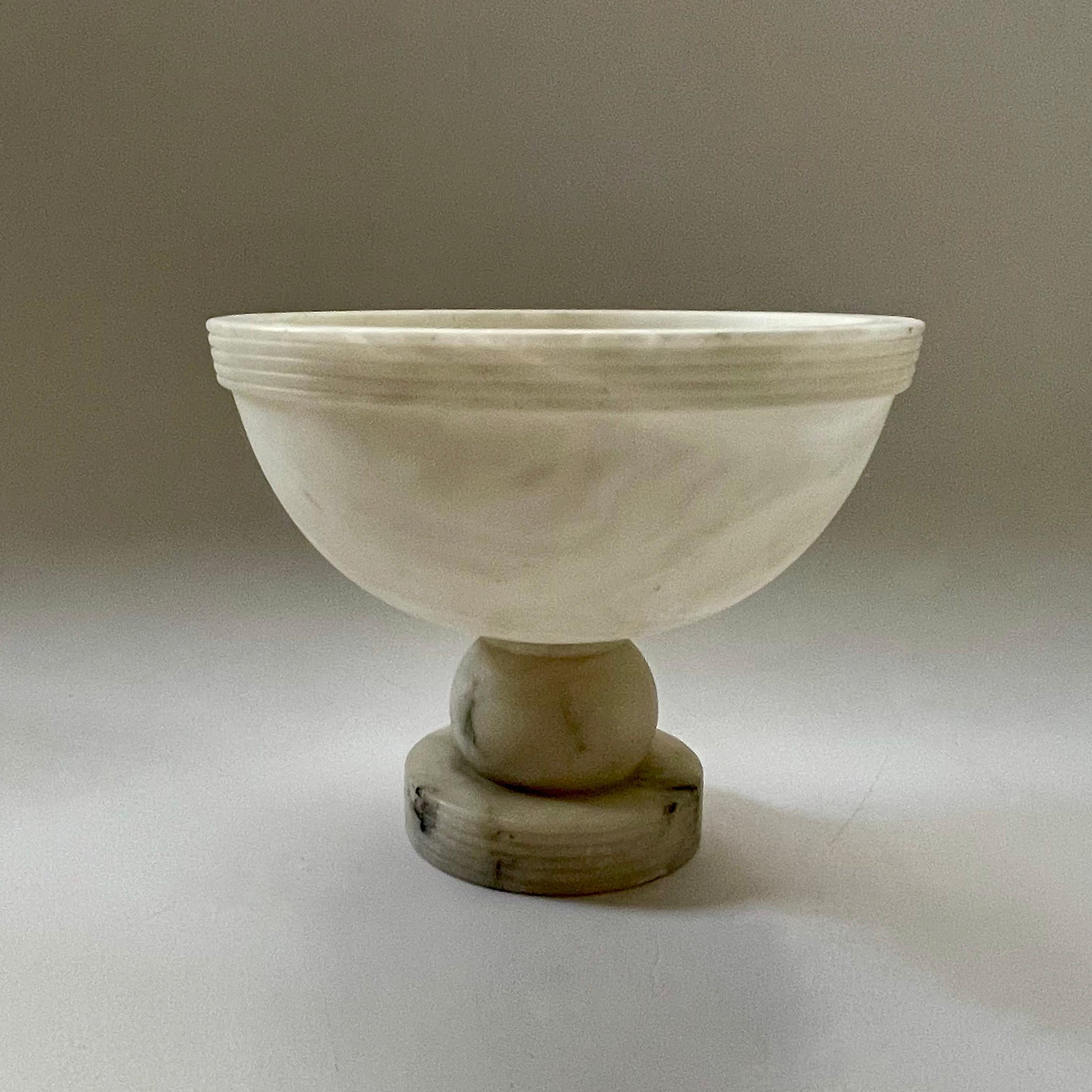 A beautiful and minimal 1930s French Art Deco alabaster centrepiece, consisting of carved alabaster forming a pedestal bowl. Raised reeding is stacked, ringing the top of the bowl and matching the round plinth base. A spherical pedestal holds up the