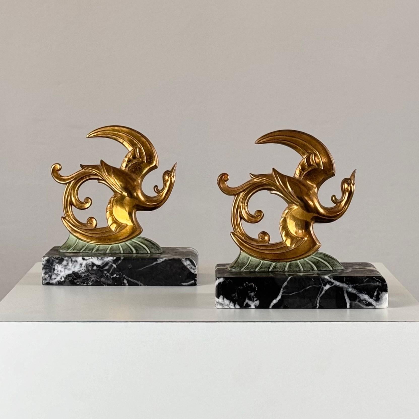 A stunning pair of French Art Deco bookends from the 1930s, masterfully crafted from luxurious black marble, gleaming brass, and finely detailed bronze. These elegant sculptures depict a pair of birds of paradise, their graceful forms captured in