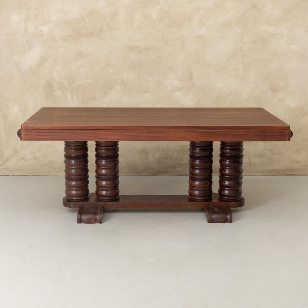 Stunning Art Deco mahogany dining table by Gaston Poisson from France, 1930s. Rectangular wood top on four chunky carved legs with pedestal base. Newly refinished dark stain shows beautiful grain. Table can extend, leaves not included. Incredible