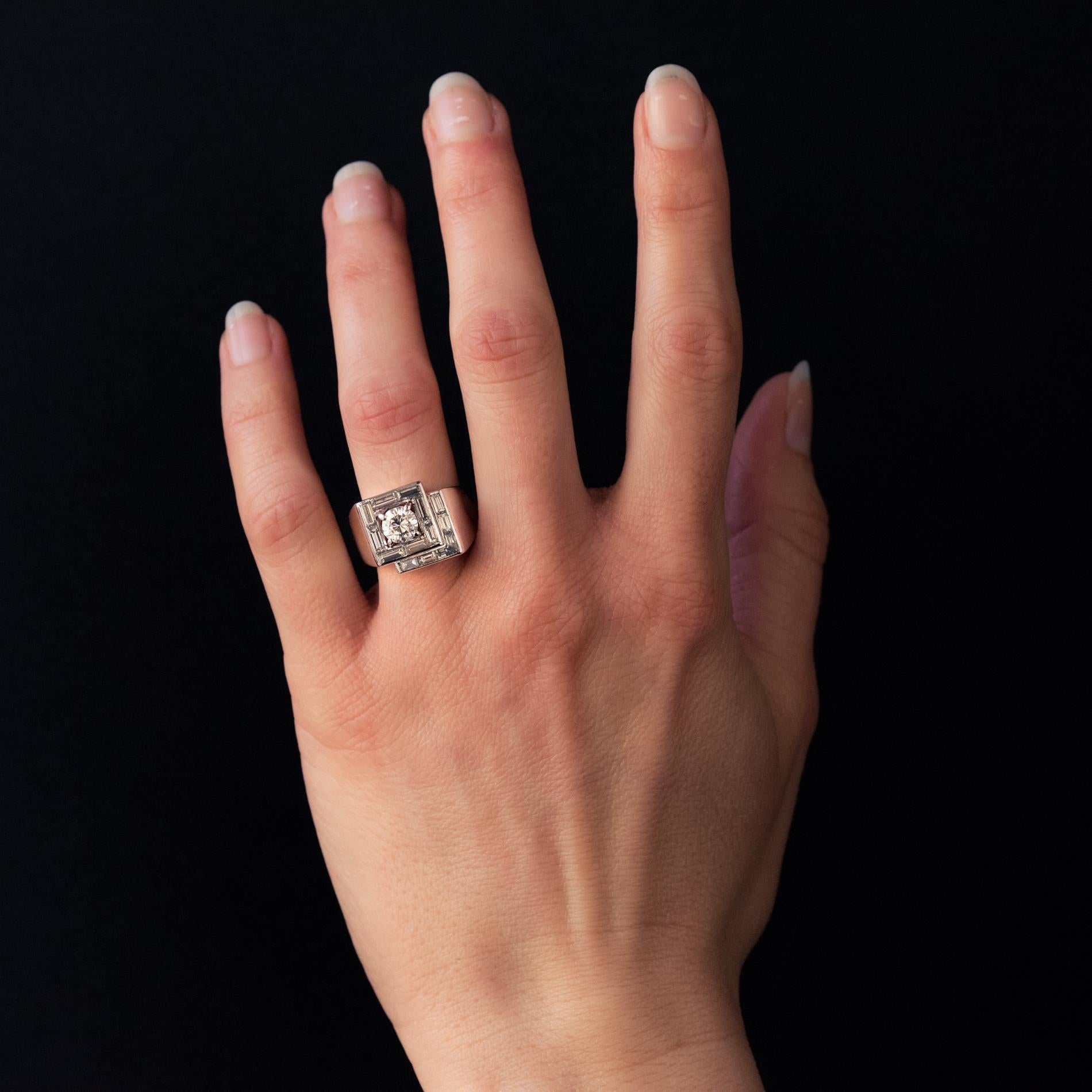 Ring aus Platin, Hundekopfpunze.
Dieser prächtige Art-Déco-Ring in quadratischer Form ist mit einem Diamanten im Brillantschliff geschmückt, der von Diamanten im Baguetteschliff umgeben ist. Asymmetrisch befindet sich darunter ein Halbquadrat, das