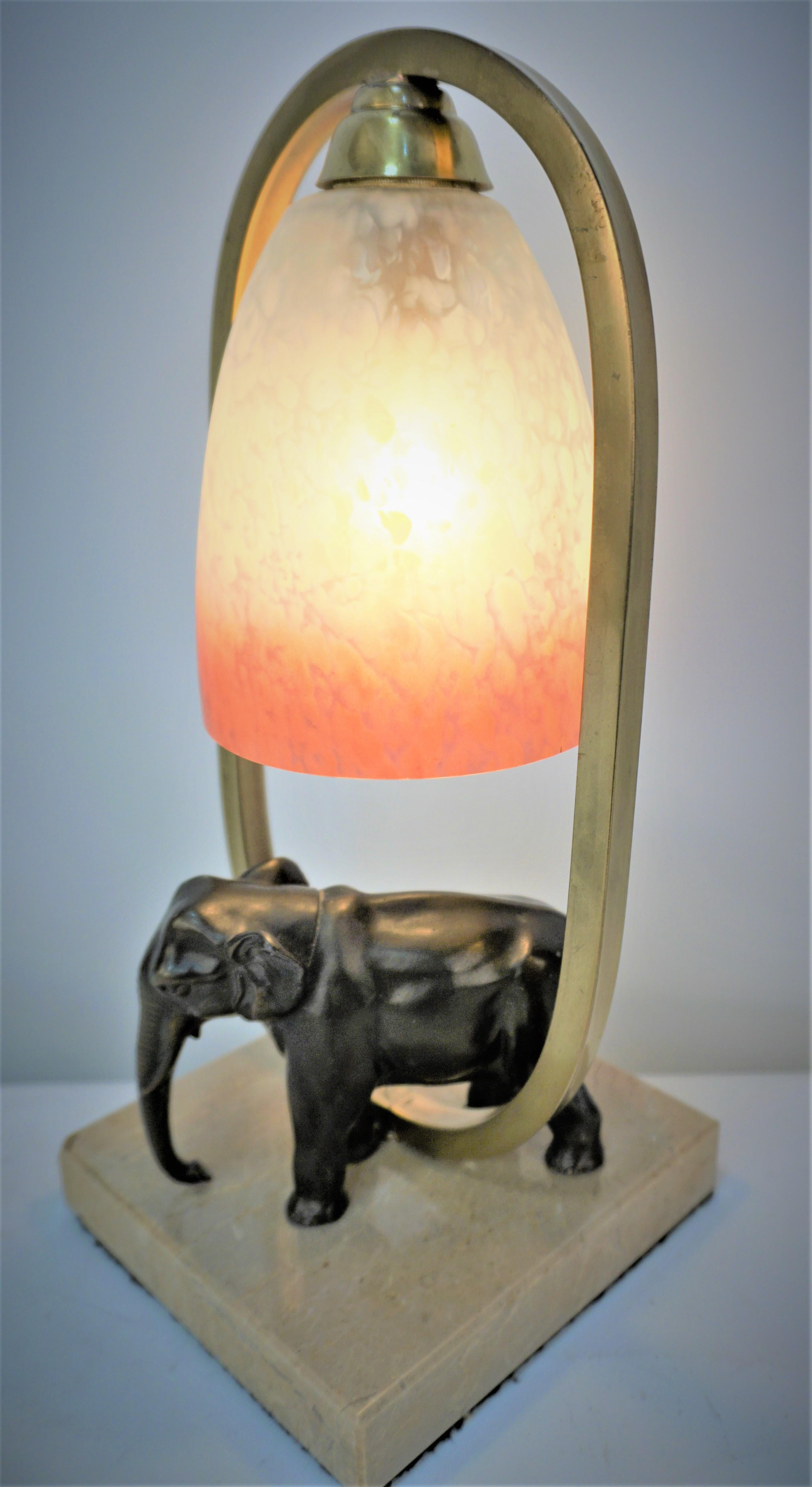 A harp shape lamp with art glass shade shining light on sculpture elephant and marble base. 