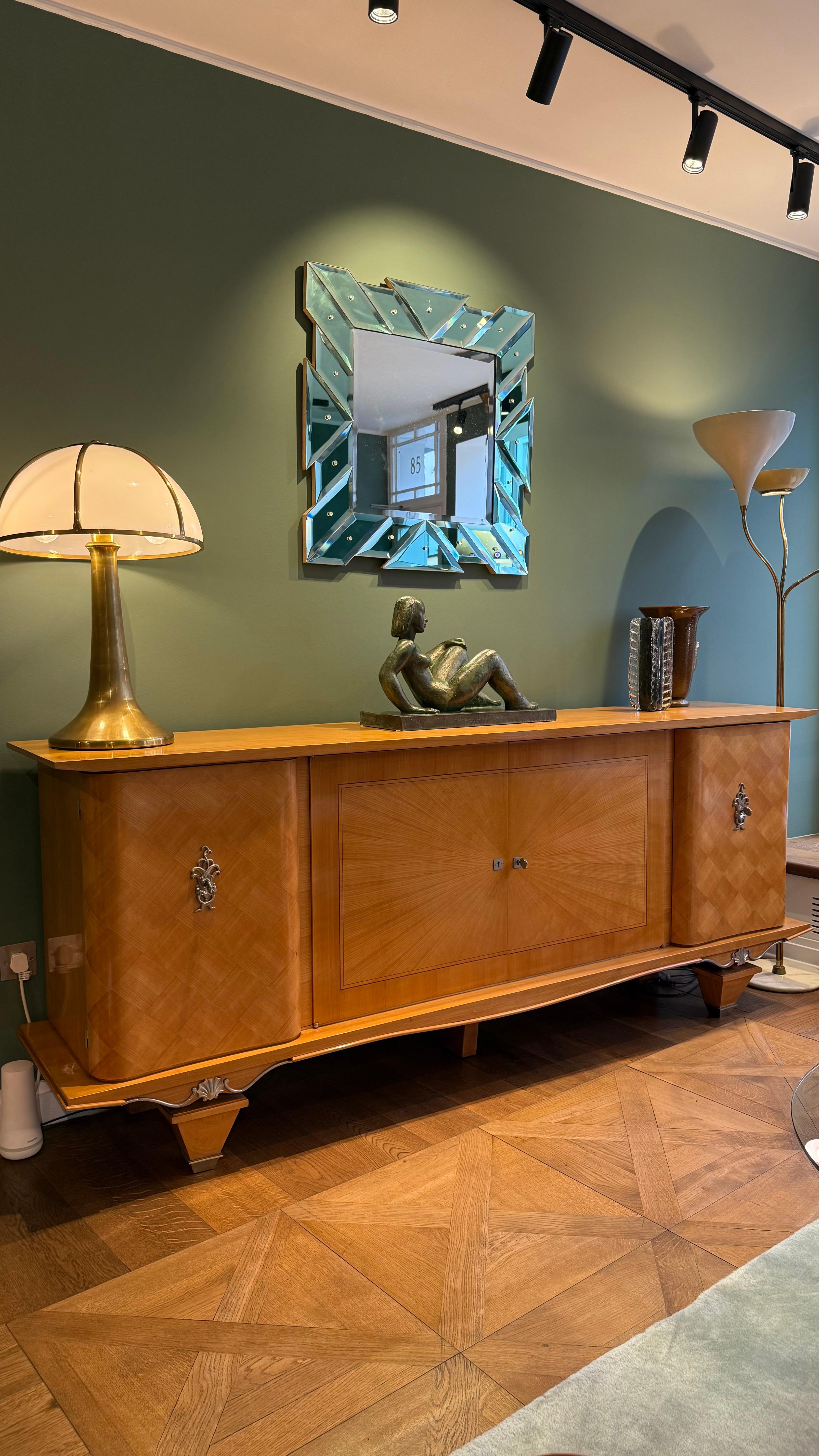 A wide and  elegant Art Deco sideboard, crafted in France circa 1930s. The piece is finely constructed in maple wood, showcasing a rich honey tone and exquisite geometric veneering that highlights the craftsmanship of the period. The central doors