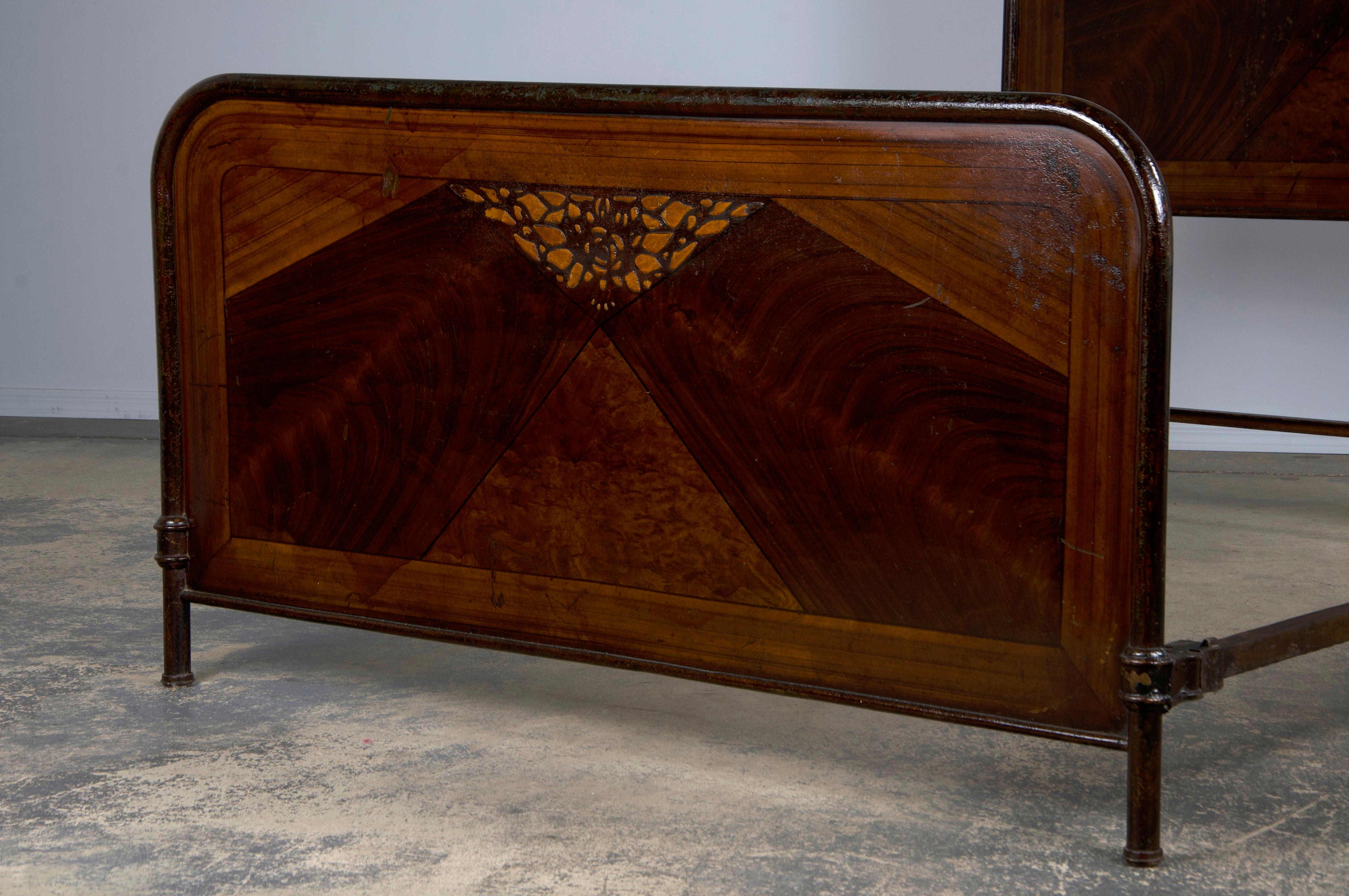 A charming 1930s French Art Deco full-size bed frame, sourced from Provence, France. Crafted from solid wrought iron, it features painted geometric designs that culminate in an elegant floral composition. The wrought iron displays a naturally aged