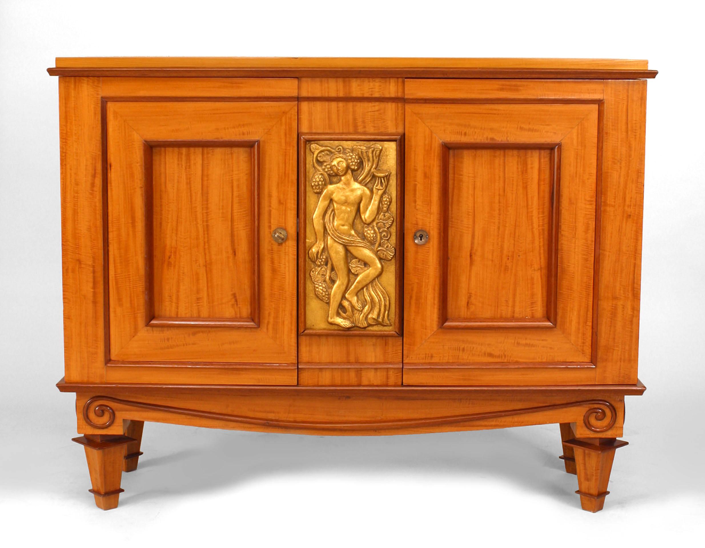 French Art Deco satinwood and mahogany with gilt trim door commode with a carved center panel with figural design. (Attributed to ATELIER ARBUS)
