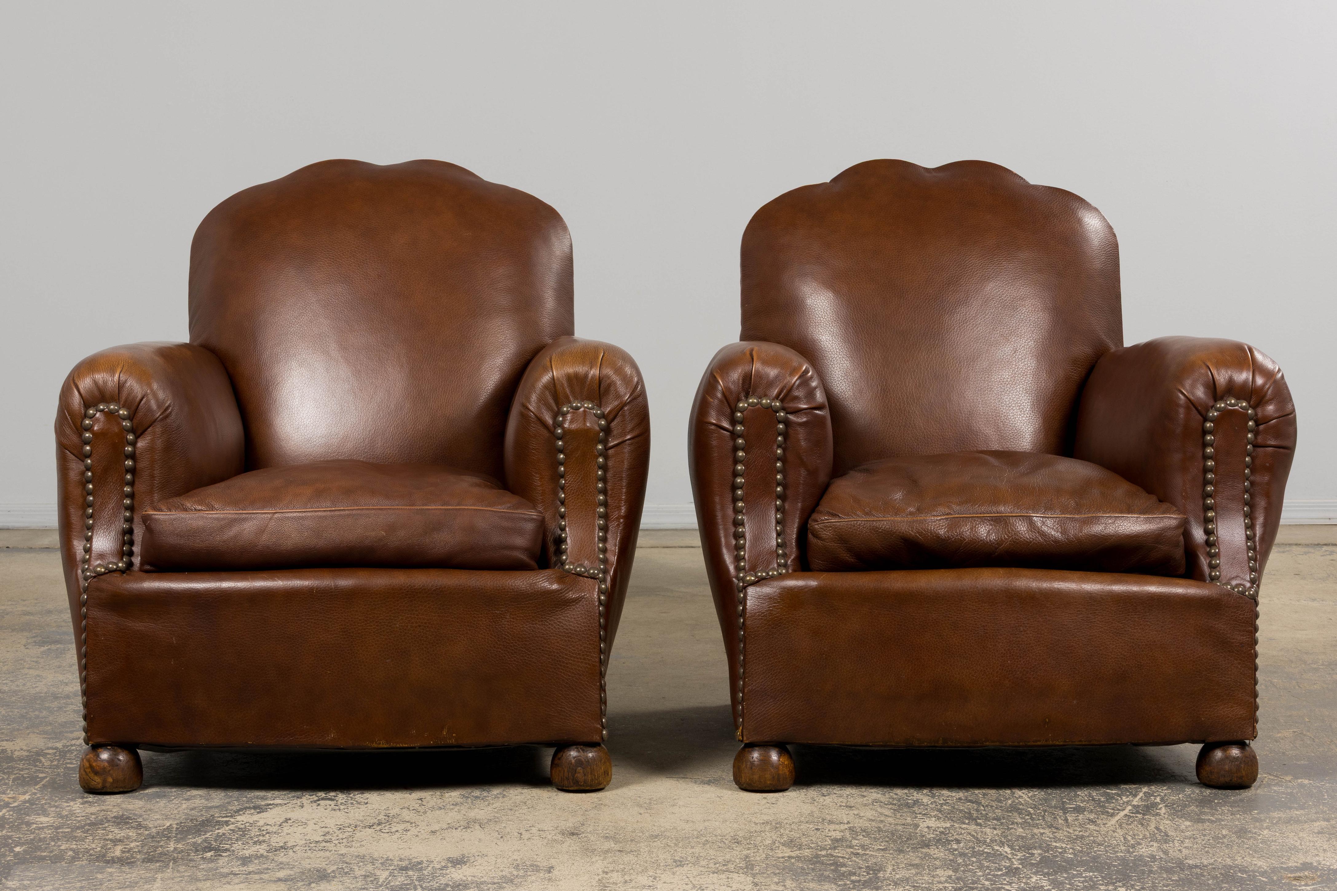 Une paire traditionnelle de fauteuils club en cuir Art déco français des années 1930 provenant de Provence, France. Ces fauteuils généreux présentent des dossiers festonnés aux silhouettes doucement arrondies, des accoudoirs roulés enveloppants et