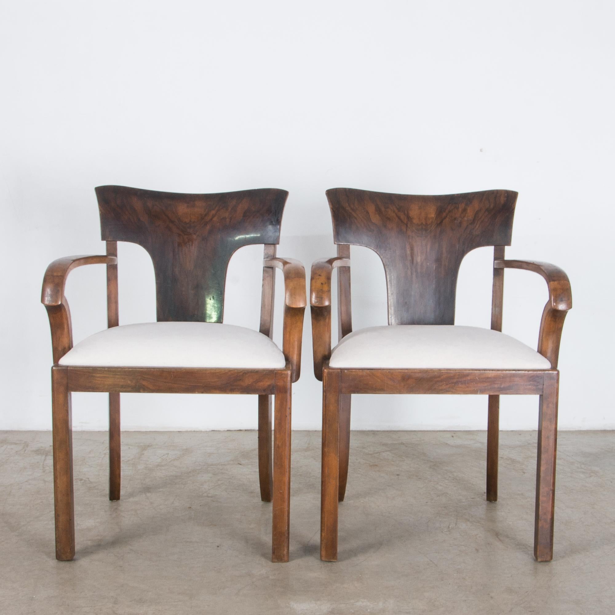 With a beautiful veneered seat back of European walnut, this pair of armchairs is composed with distinctive Art Deco style. Elegant bentwood arms and rounded shapes give a simple elegance, a reminder of luxury. A sleek and streamlined shaped suggest
