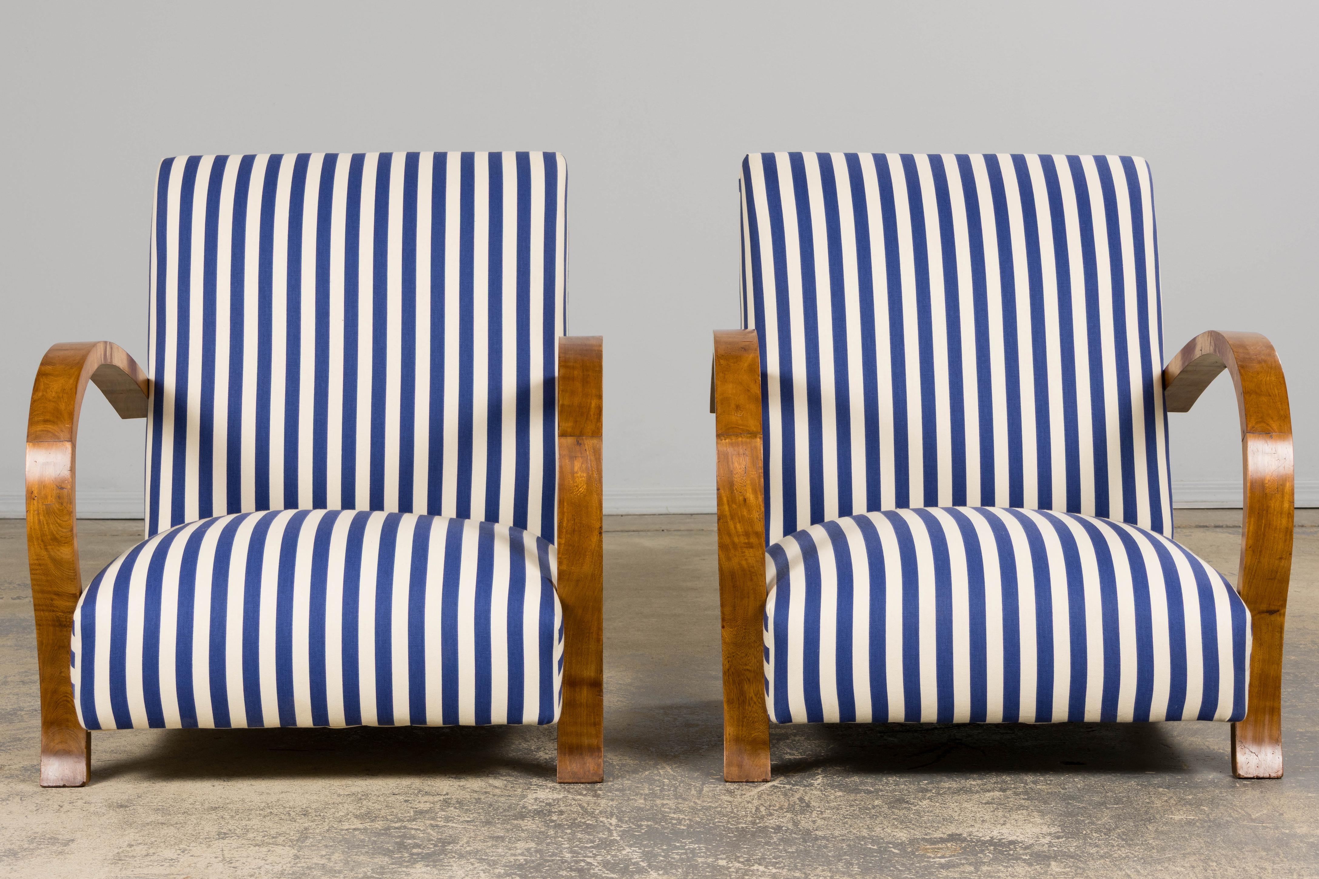 A handsome and refined pair of late 1930s French Art Deco lounge chairs, sourced from Provence, France. Each chair is hand-crafted with a solid wood frame and features elegant curved bridge arms in solid walnut, reminiscent of the Jindřich Halabala
