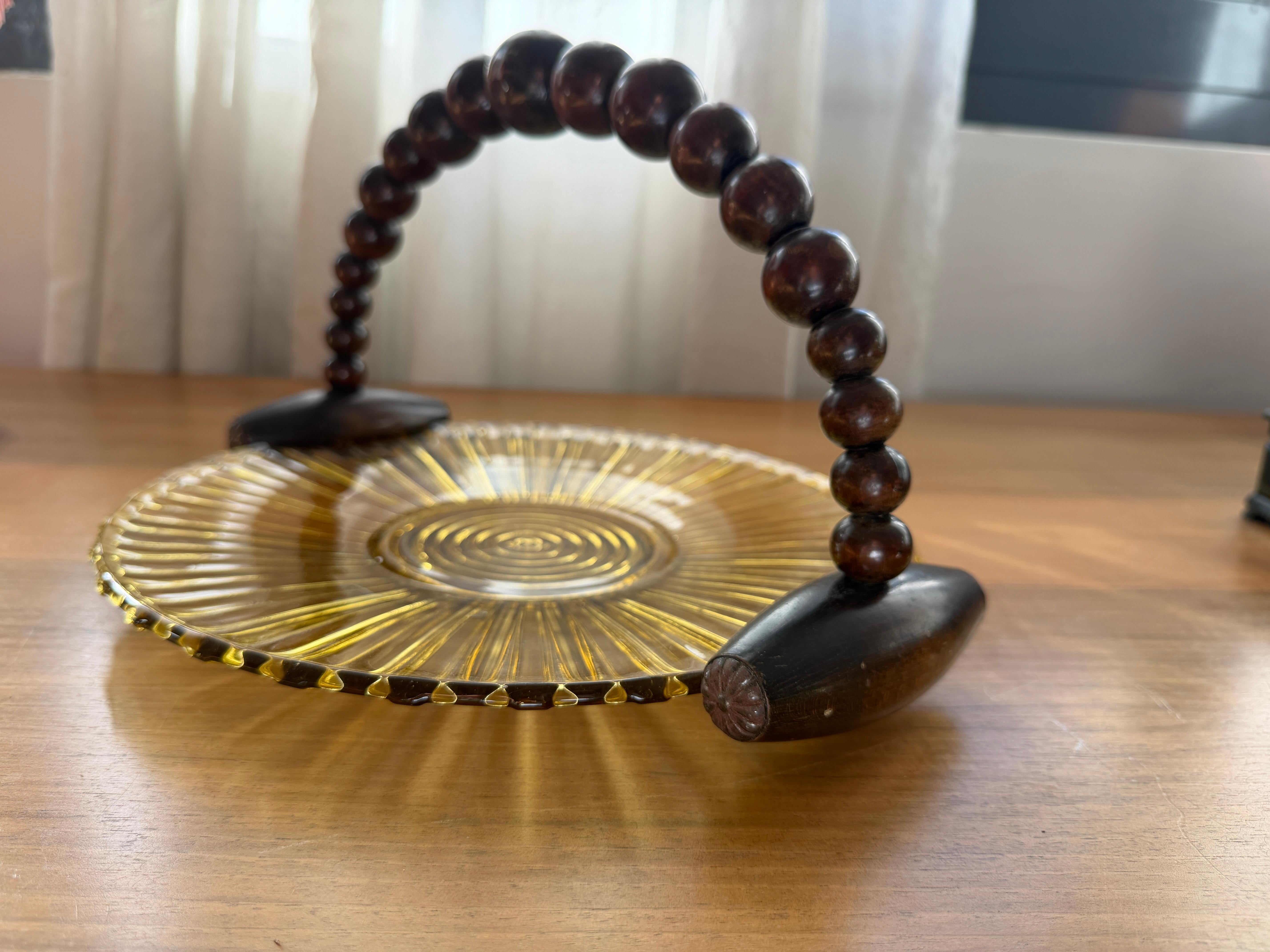 Sunburst ribbed amber glass with hand-gilded rings, finished with a beaded wooden swing handle on carved terminals. Beautiful for petits fours, fruit, or as a sculptural decorative piece - the handle folds flat when not in use.

Why we love it
Art