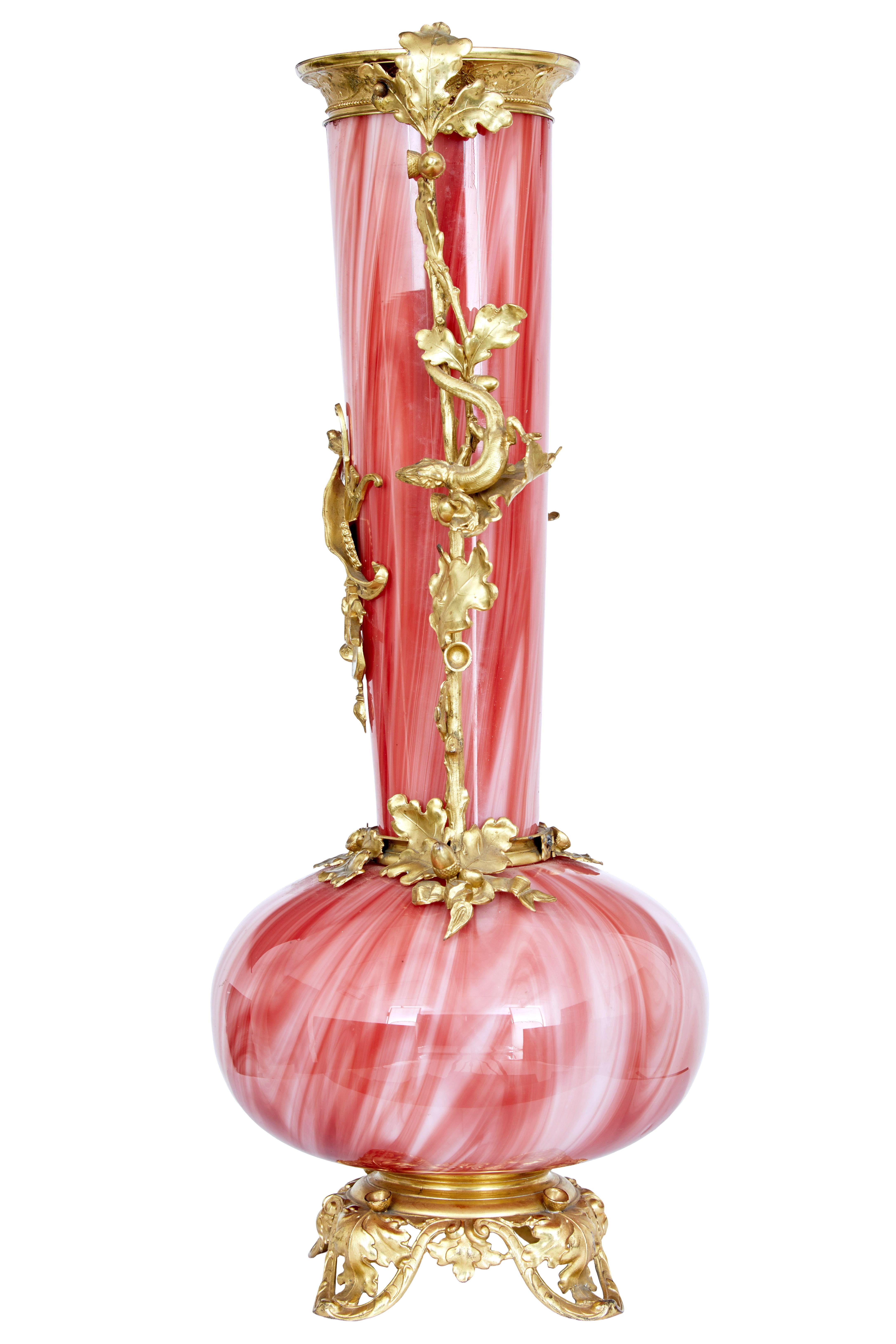 1930's French art glass vase with ormolu mounts circa 1930.

Elegant hand blown art glass of reds and whites, profusely decorated with ormolu mounts to the rim, top and base.   Decorated with acorns and oak leaves down the stem with musical themed