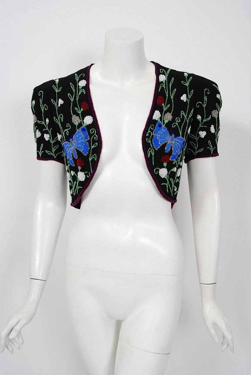 This sensational 1930's French bolero jacket is lavishly embellished with colorful glass beadsthroughout. The highly stylized butterfly garden novelty motif perfectly captures the aesthetic during this time period. So very Elsa Schiaparelli.