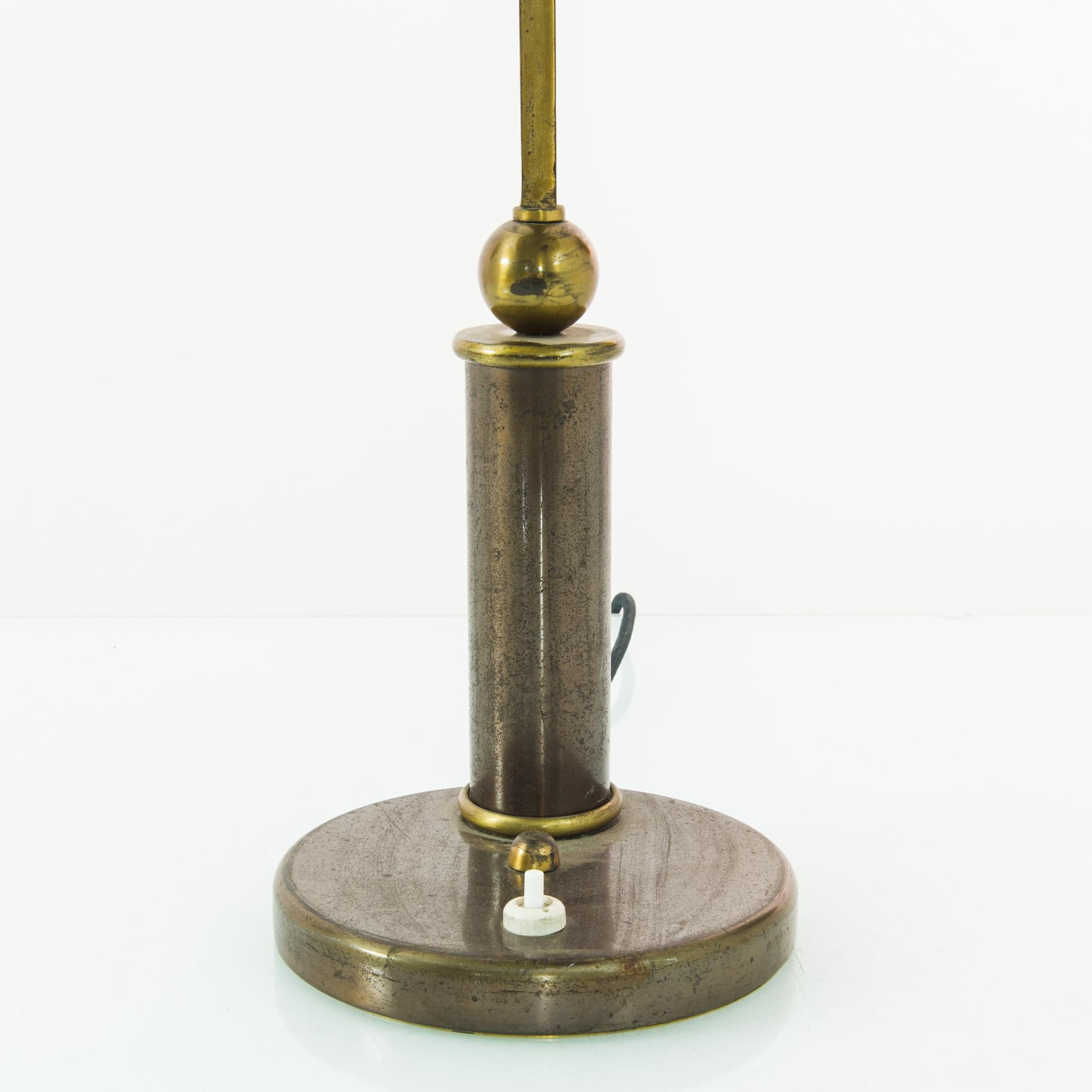 This metal table lamp was made in France, circa 1930. The generously sized dome lampshade, circular fixtures, and the globe balanced precisely on the cylindrical stand give it a geometric silhouette, hinting at an Art Deco influence. With its