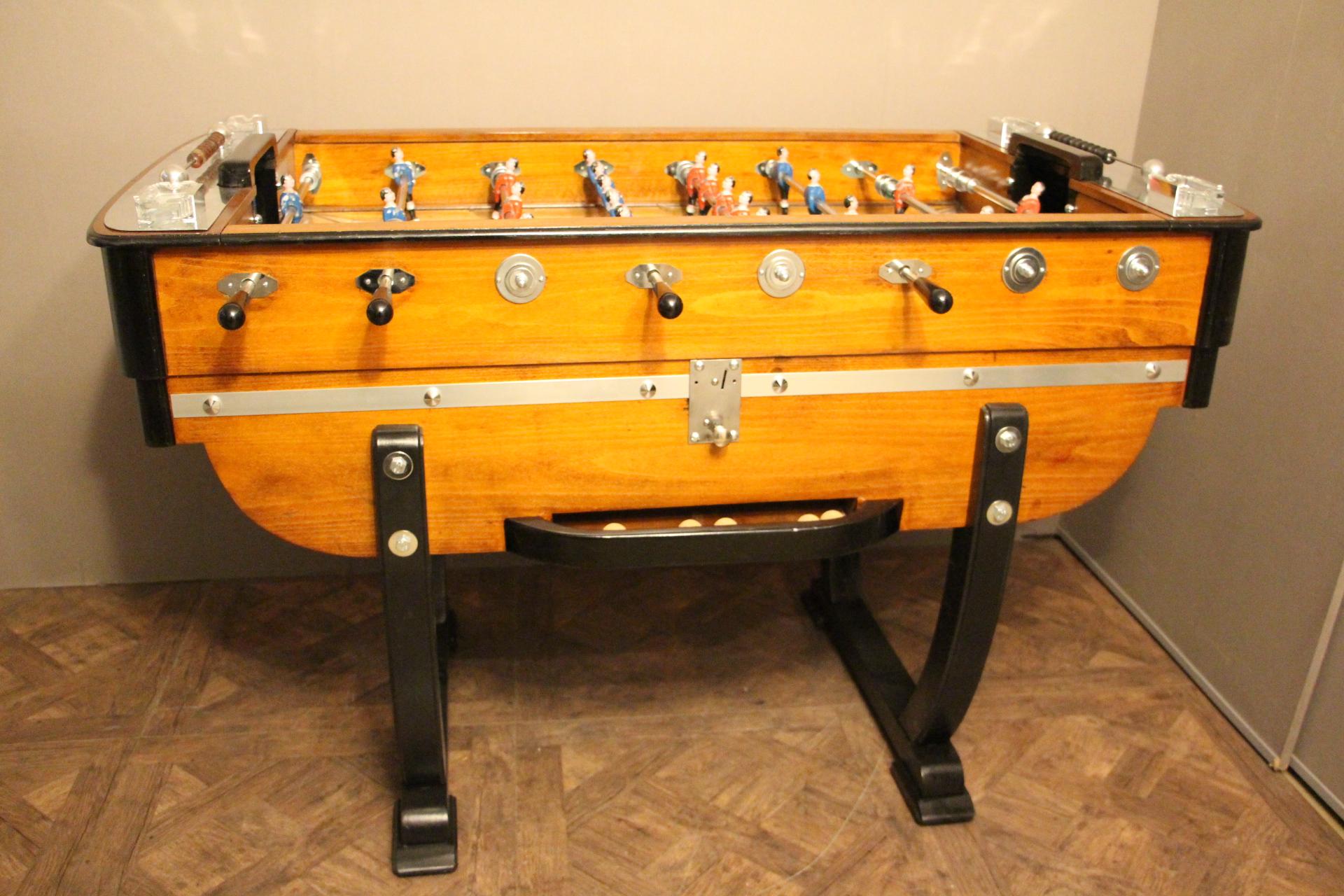 This piece is really out of the ordinary.
It is raised on black stylized lyre-shaped end supports. This French beechwood and ebonized table has got red and blue players, green playing field , four Lalique crystal ashtrays and polished aluminium