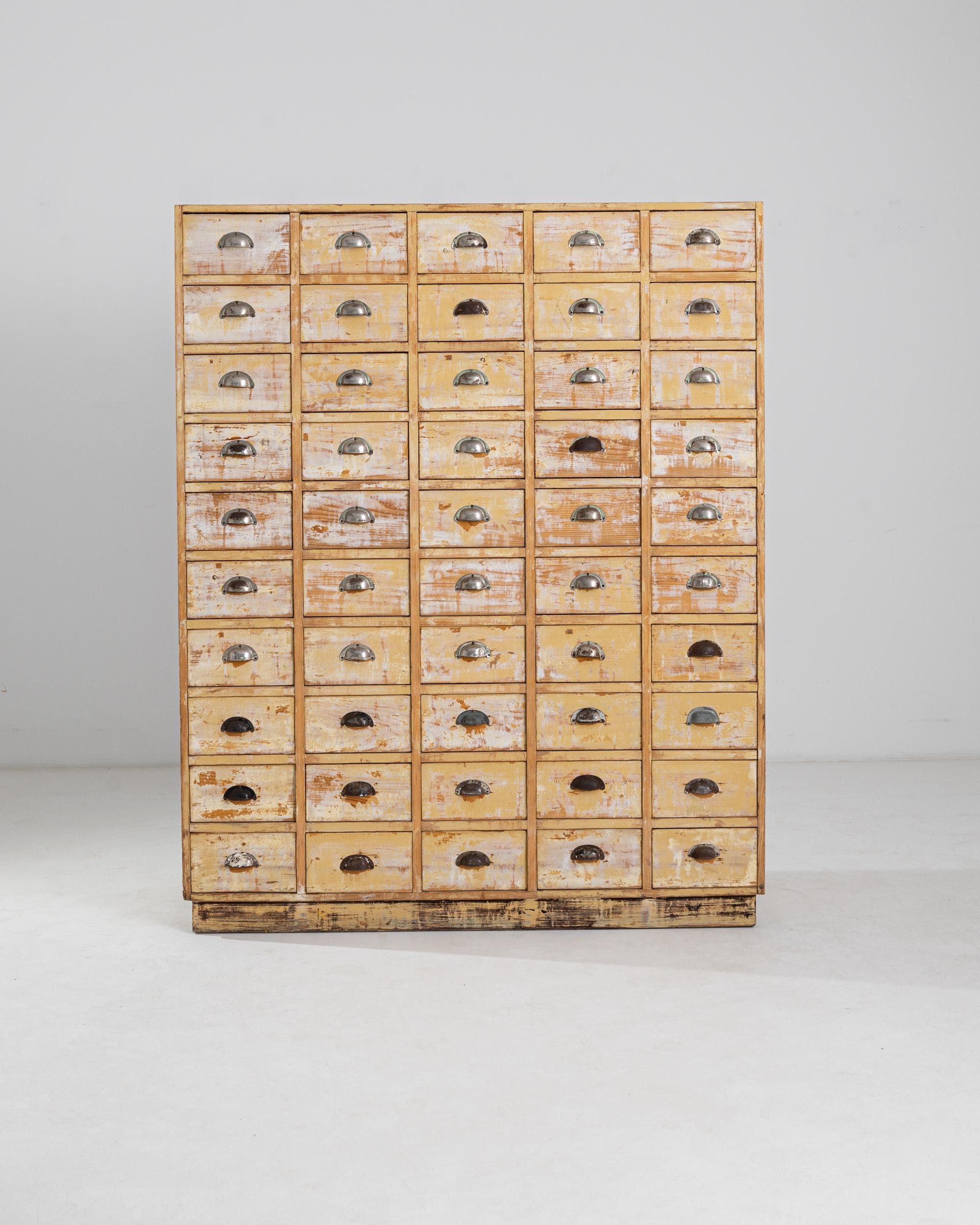 An eye-catching Industrial period piece, this wooden chest of drawers would have originally been used in a workplace for storing files, index cards, or parts. Made in France in the 1930s, the case houses an array of 50 small drawers, arranged in a