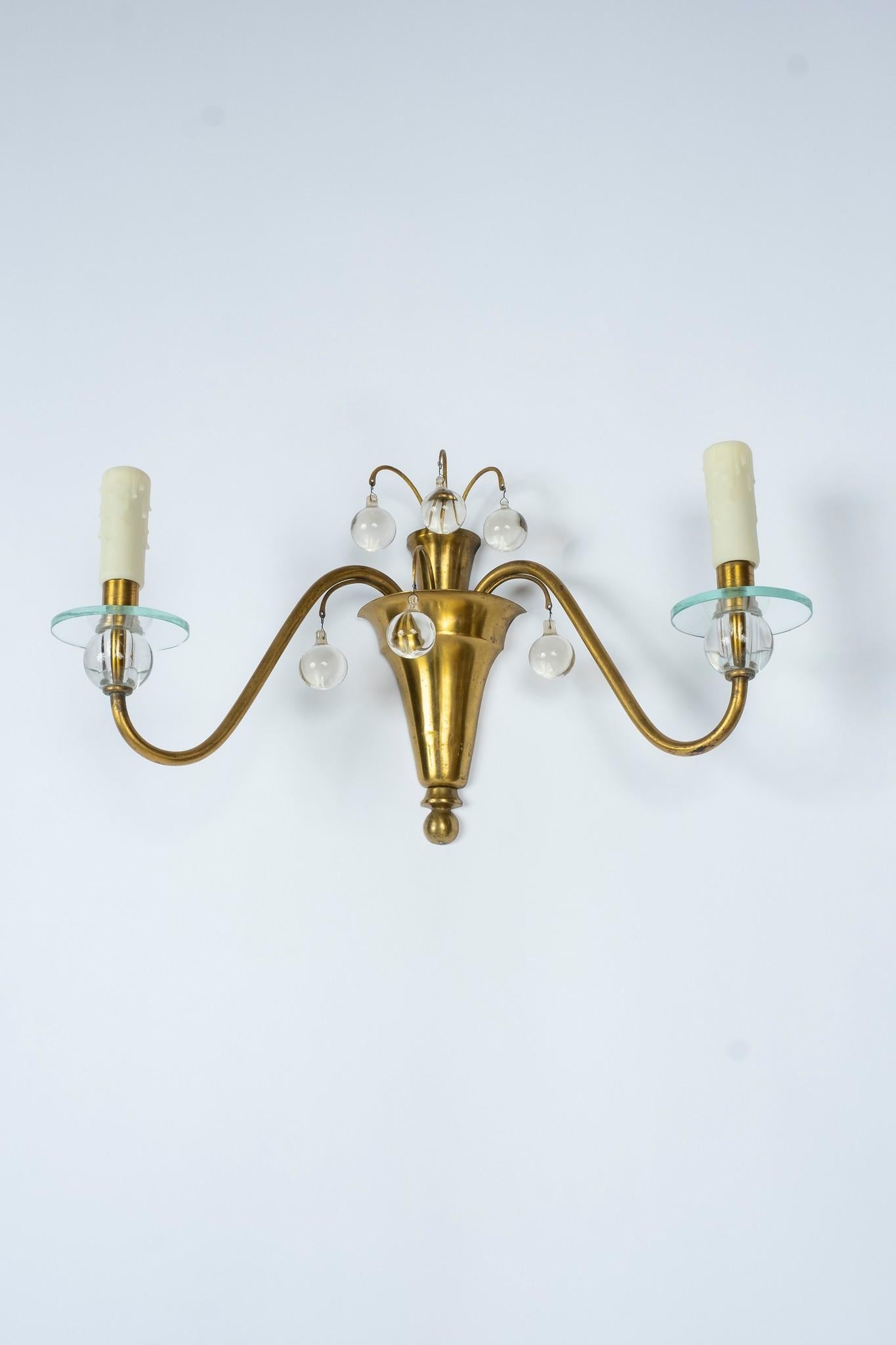 A pair of 1930s two-arm French brass sconces. Details include hanging crystal ball pendants and glass spheres that support each bobèche. These sconces are a modern contemporary design indicative of the Deco era.