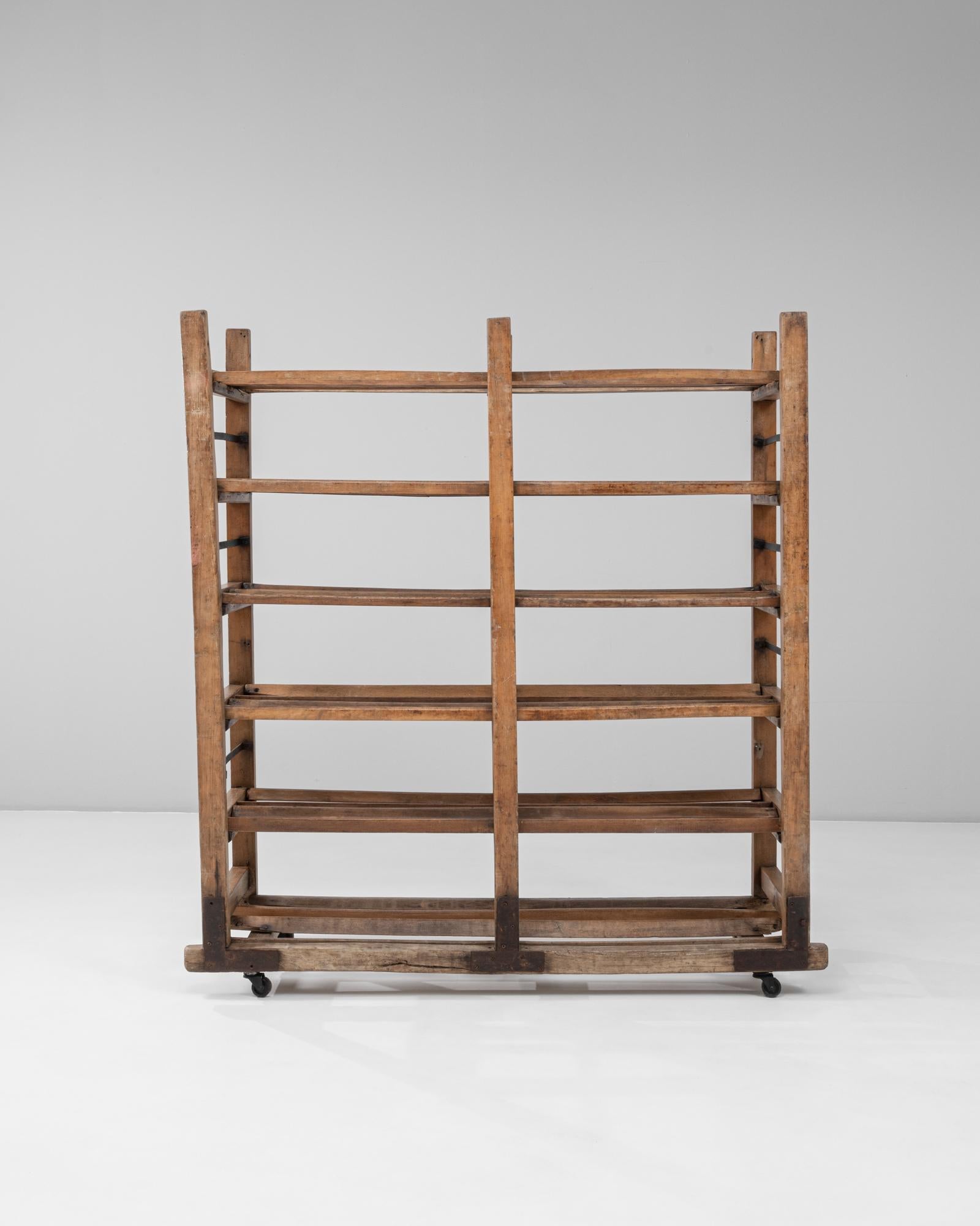 This 1930s French industrial bakery rack on wheels is a rare surviving example of early commercial craftsmanship, combining utilitarian design with the warm character of aged wood. Constructed from solid timber with original iron braces, the rack