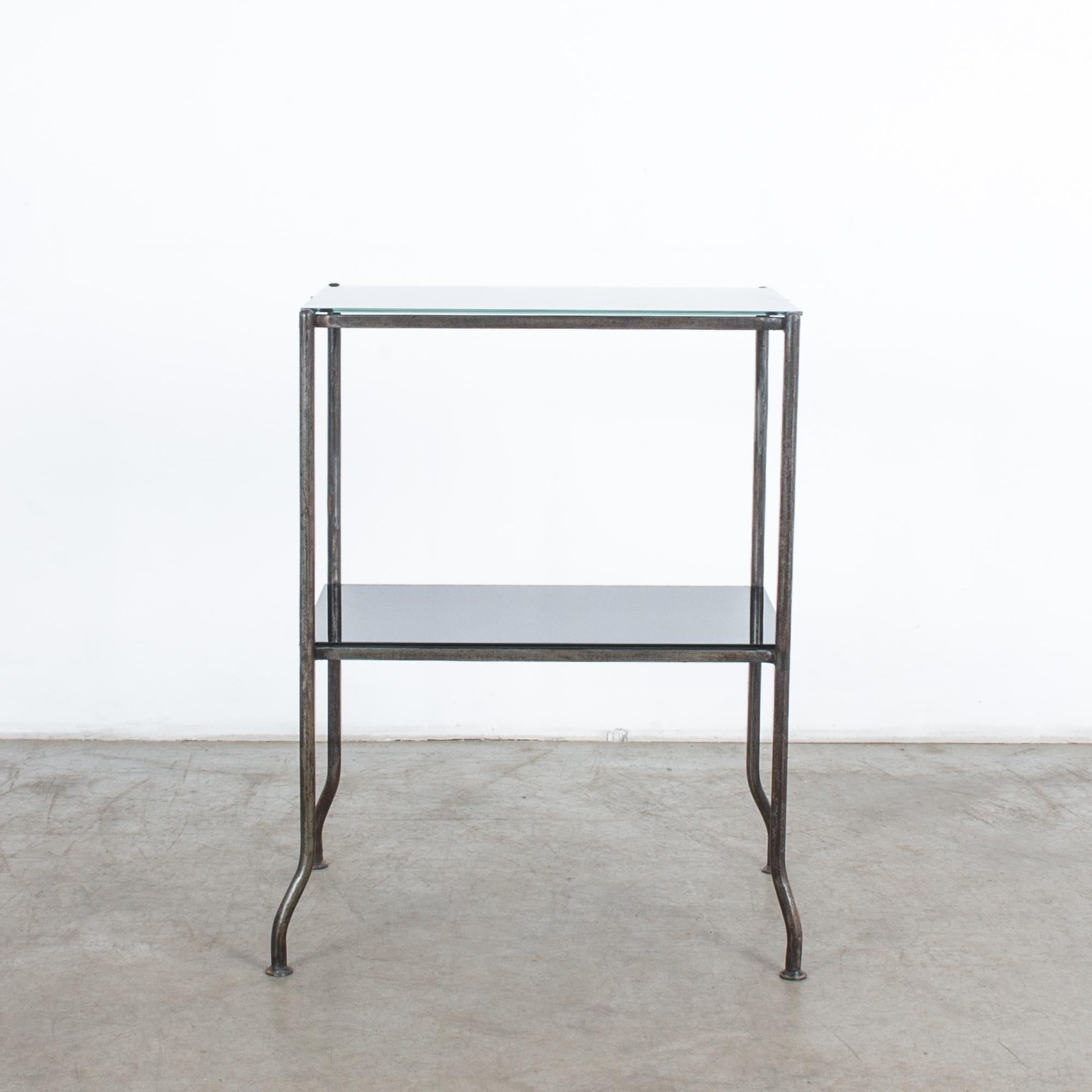 This metal table from France, circa 1930, has a simple rectangular metal frame and two-tiered tabletops made of black glass. Knock-kneed feet add a playful touch to the linear silhouette. The polished black glass gives this table a sleek and stylish