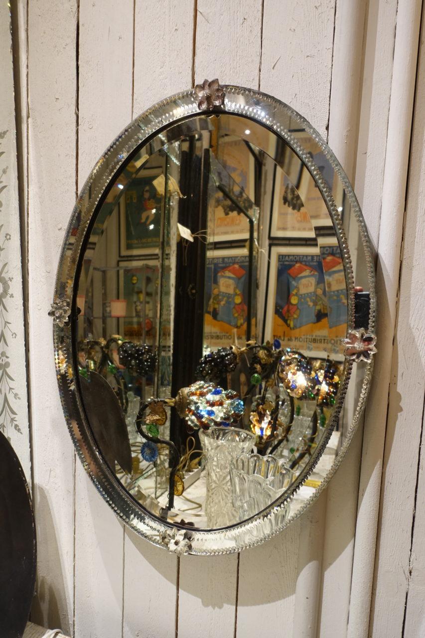 Beautiful vintage oval Venetian mirror, with a lovely patina in the facet cut mirror glass. Dating back to 1930s France. Note the elegant and thin faceted frame around the mirror itself as well as the charming small flower rosettes covering the