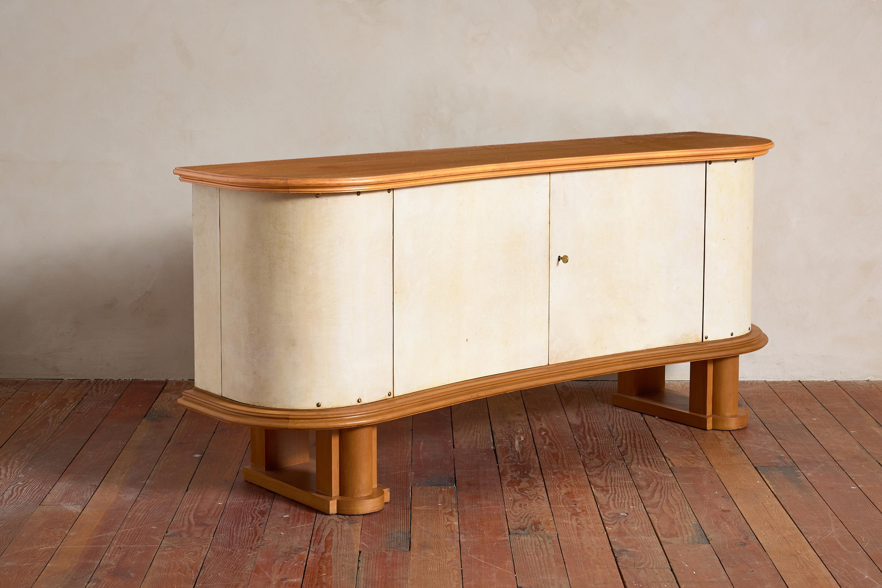 Stunning Art Deco parchment sideboard with curved lines and gorgeous patina.  France, circa 1930s

Curved original parchment doors open from the corners to reveal open shelving and center doors open for shelving and drawers. 

Brass stud detailing.