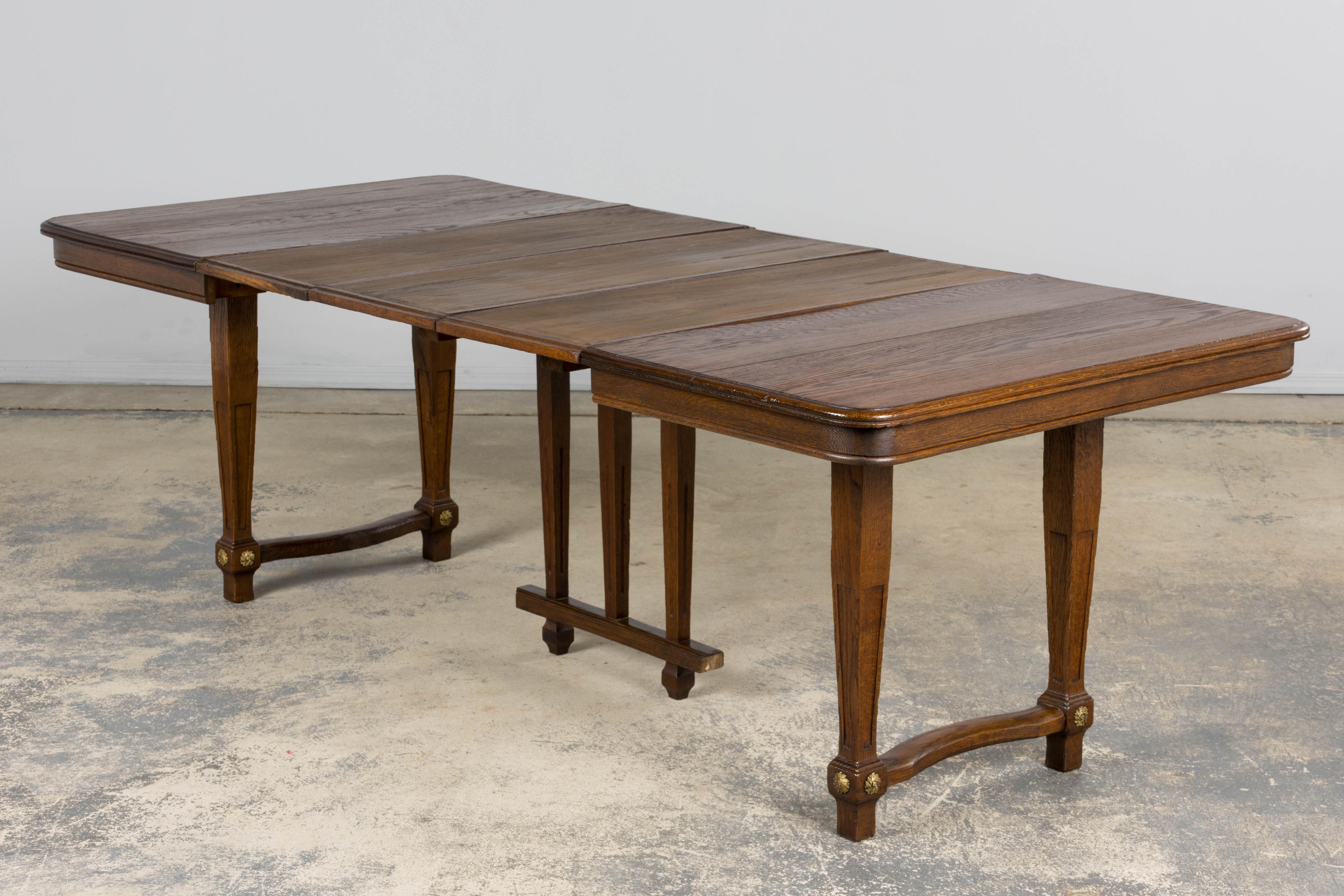 An elegant French Art Deco oak extendable dining table, circa 1930s, sourced in Paris. The rectangular top with softly rounded corners is raised on four tapered legs, each joined by shaped stretchers and adorned with gilt-bronze rosettes at the