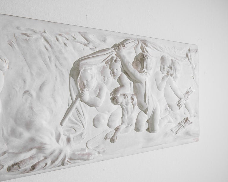 A relief sculpture made of plaster, produced in France circa 1930. A dreamlike scene of waddling toddlers out in the woods, playing unsupervised: doing everything from sleeping in the brush to making fire. The purity of the moment captured in white