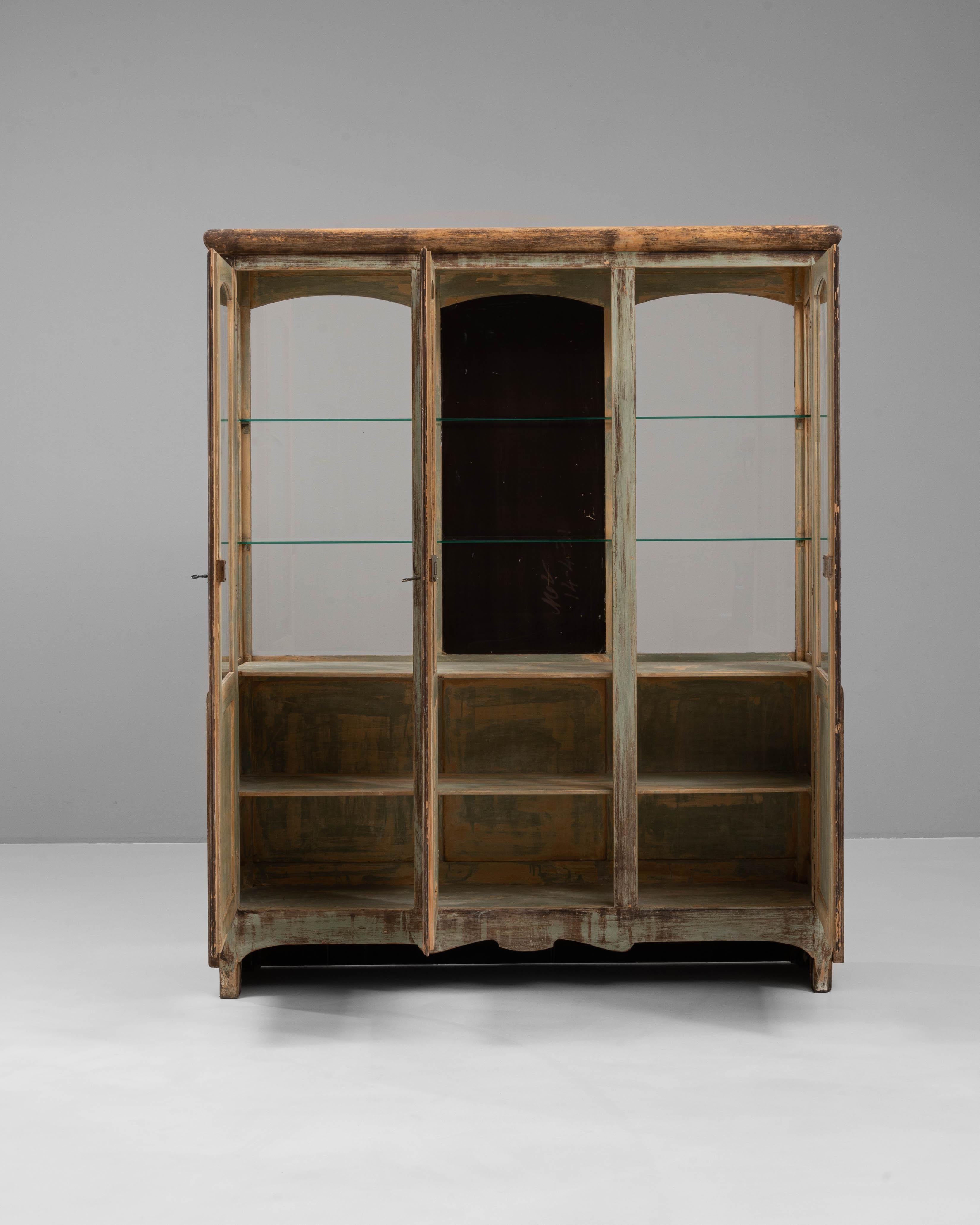 This 1930s French store vitrine exudes rustic charm and functionality, making it an elegant piece for displaying treasured items. The wooden frame, adorned with a distressed green finish, showcases an aged patina that reflects its storied history.