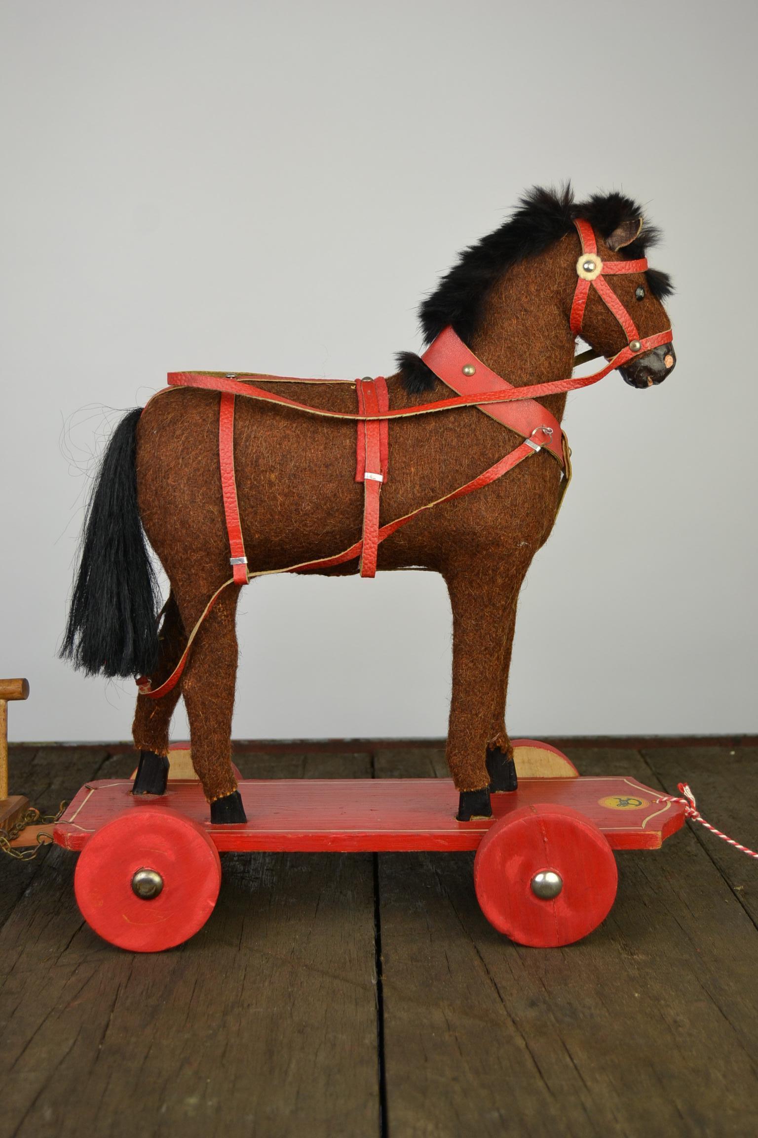 Beautiful antique German Roy,
a pull toy, a pull horse toy with cart.
This antique toy horse, circa 1930s, is mounted on a wooden platform with wheels. The carved wood horse is covered with brown burlap.
The hooves and snout are hand carved and