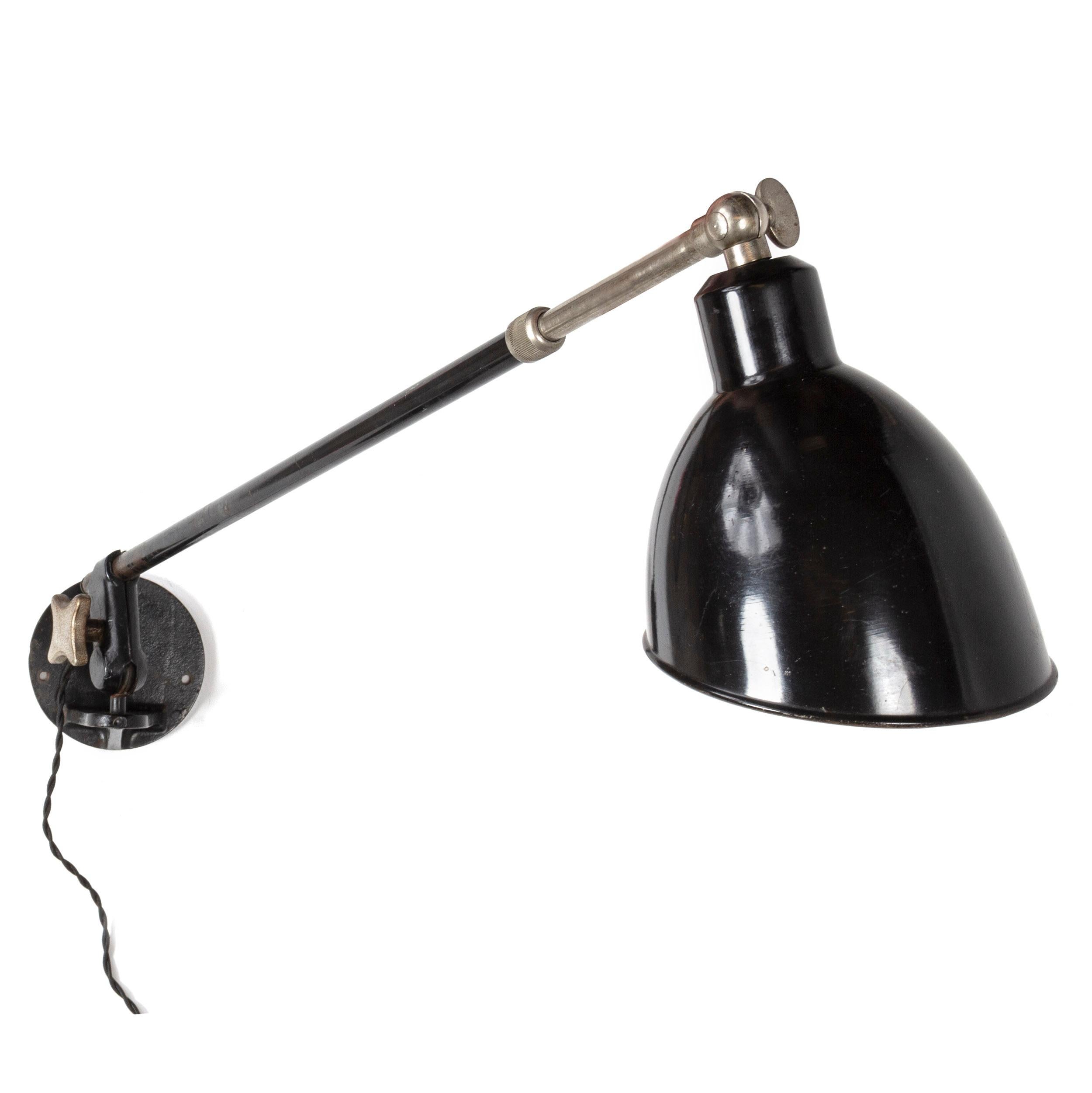 A telescoping industrial wall lamp with a pivoting bracket and adjustable arm supporting a black enameled steel shade.