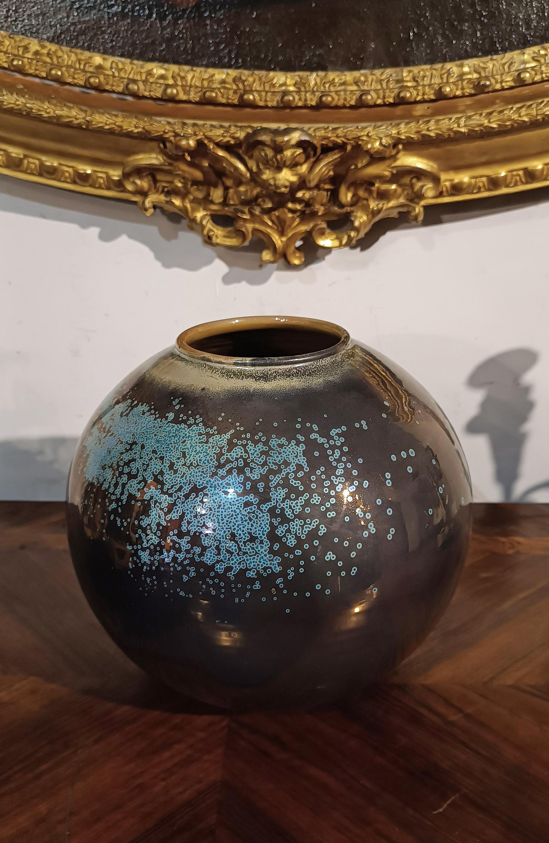 Magnifique vase rond en céramique émaillée, avec des reflets bronze et des décorations avec des éclats de couleur vert d'eau. Le vase a également un bord arrondi et légèrement évasé et un fond en forme d'anneau. Les 