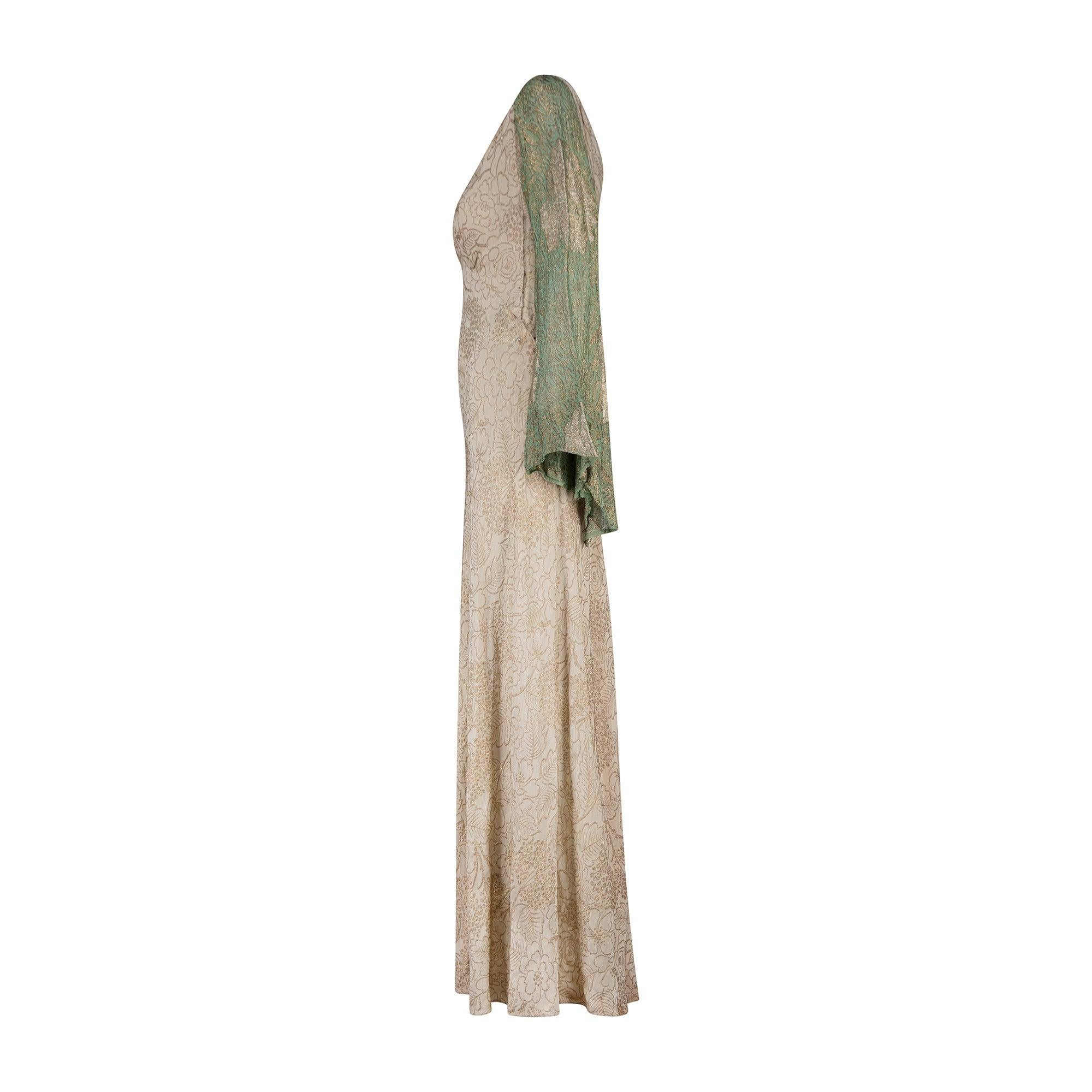 This outstanding 1930s lamé evening dress is cut to a classic bias-cut silhouette and has a gentle V-neck and full skirt that swirls around the ankles. The fabric is mesmerising, a burnished pale gold detailed all-over with intricate lamé embroidery
