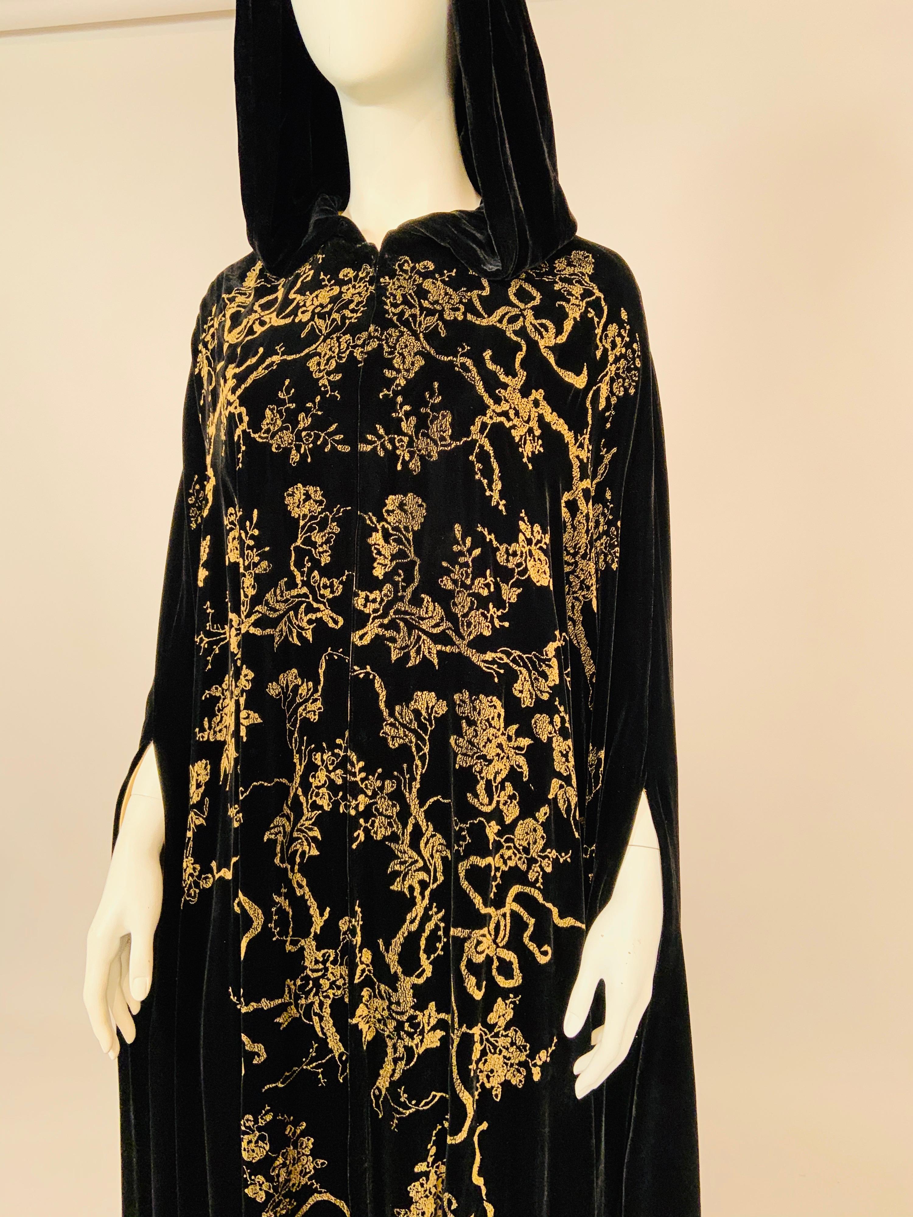 This dramatic gold stenciled black silk velvet hooded cape is designed in the style of Fortuny and Gallenga, who were both famous for their stenciled velvet and cotton garments in the first half of the 20th century. it dates to the 1930's and   has