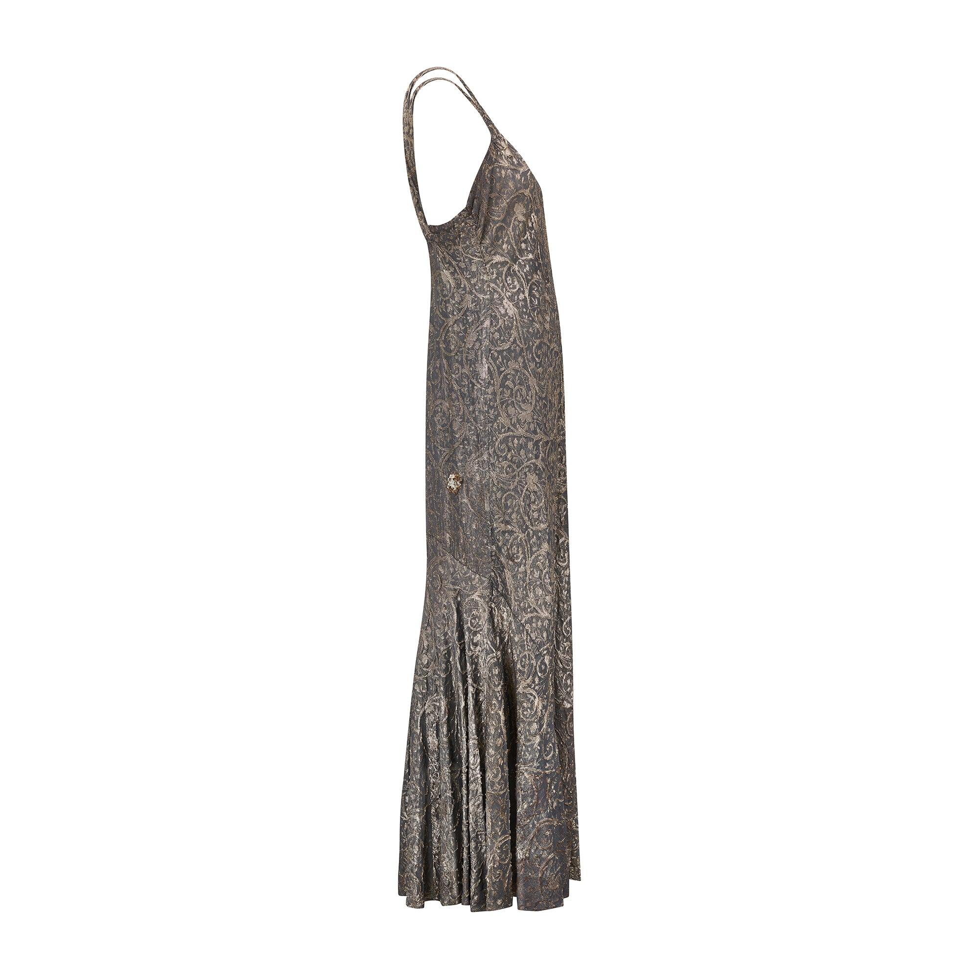 Este llamativo vestido de los años 30 está confeccionado en lamé de color azul gris pizarra, con un brillante tejido metálico plateado y dorado que revela un tema botánico y floral. El corte al bies en el tobillo crea una silueta atemporal y ceñida