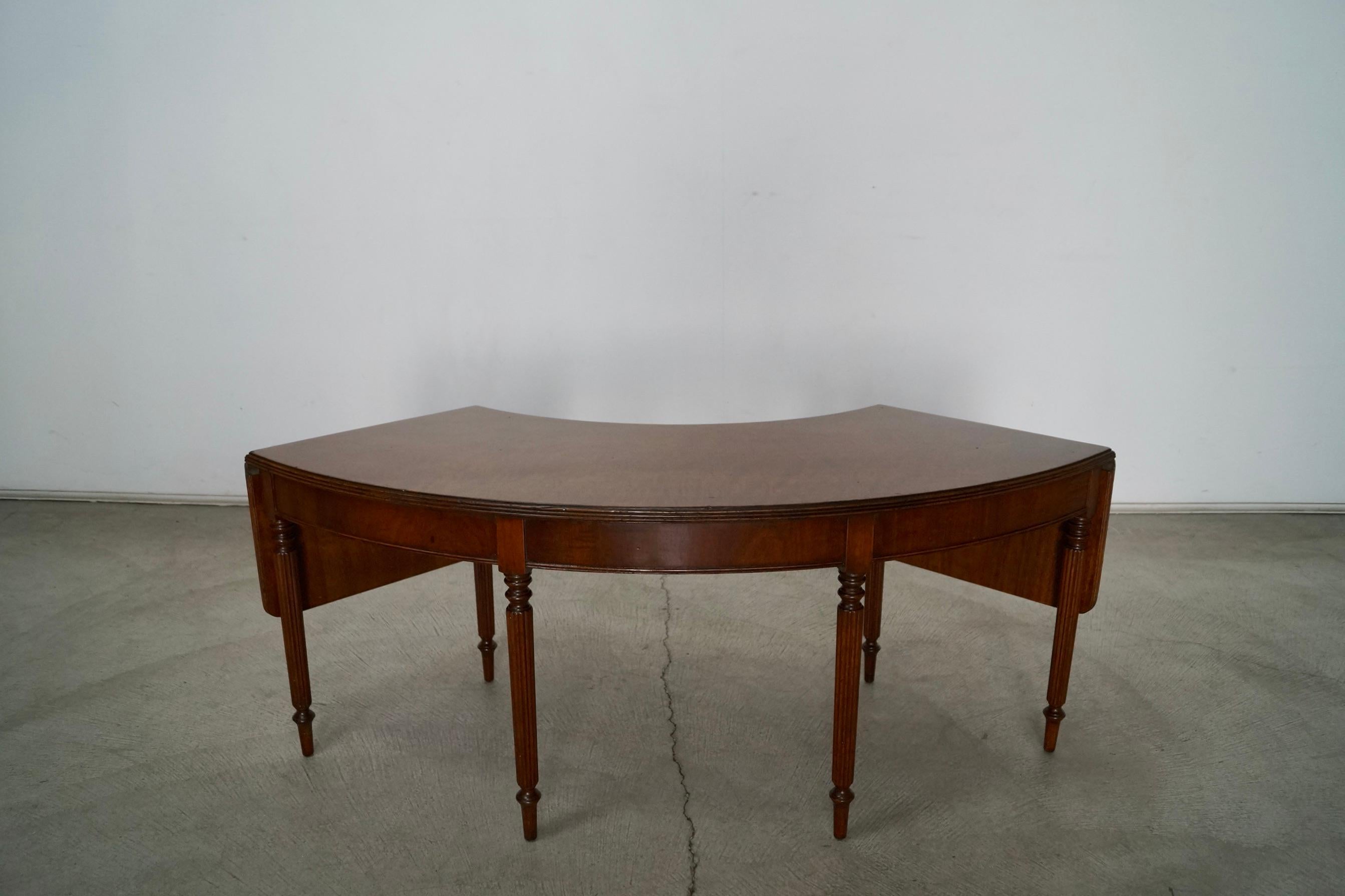 Antique coffee table for sale. Special table that has a half-moon shape and has leaves on either side that extend out. Great design, and in great vintage condition. Made of mahogany with a walnut finish. Has six fluted legs. Has serial number and