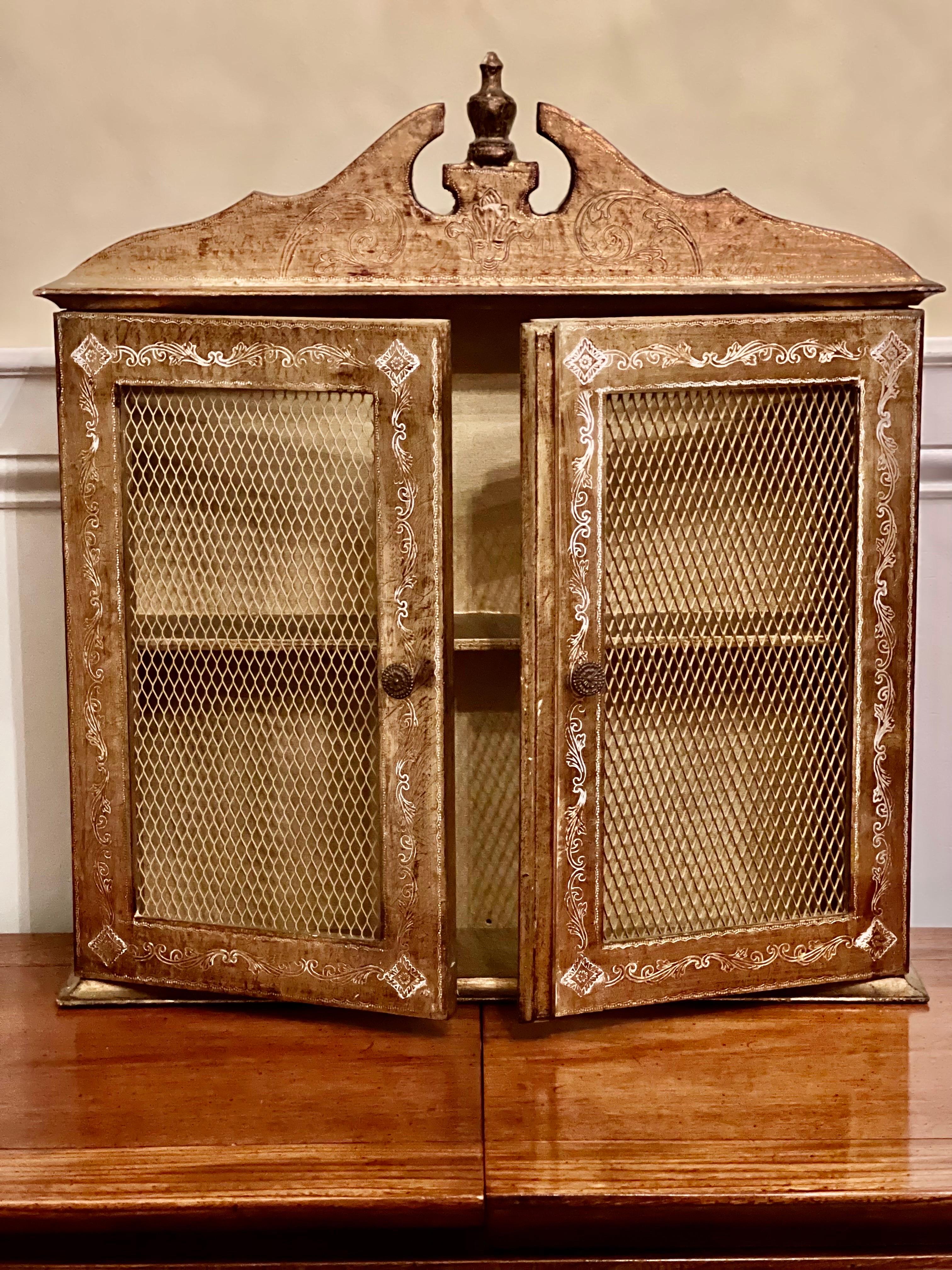 Lovely vintage handcrafted Italian wall cabinet with gold gilt finish and Florentine detail throughout by Florentia, c1930's Italy. Intricate hand painted and carved white foliate scroll motif adorns the sides and front. Doors have detailed round