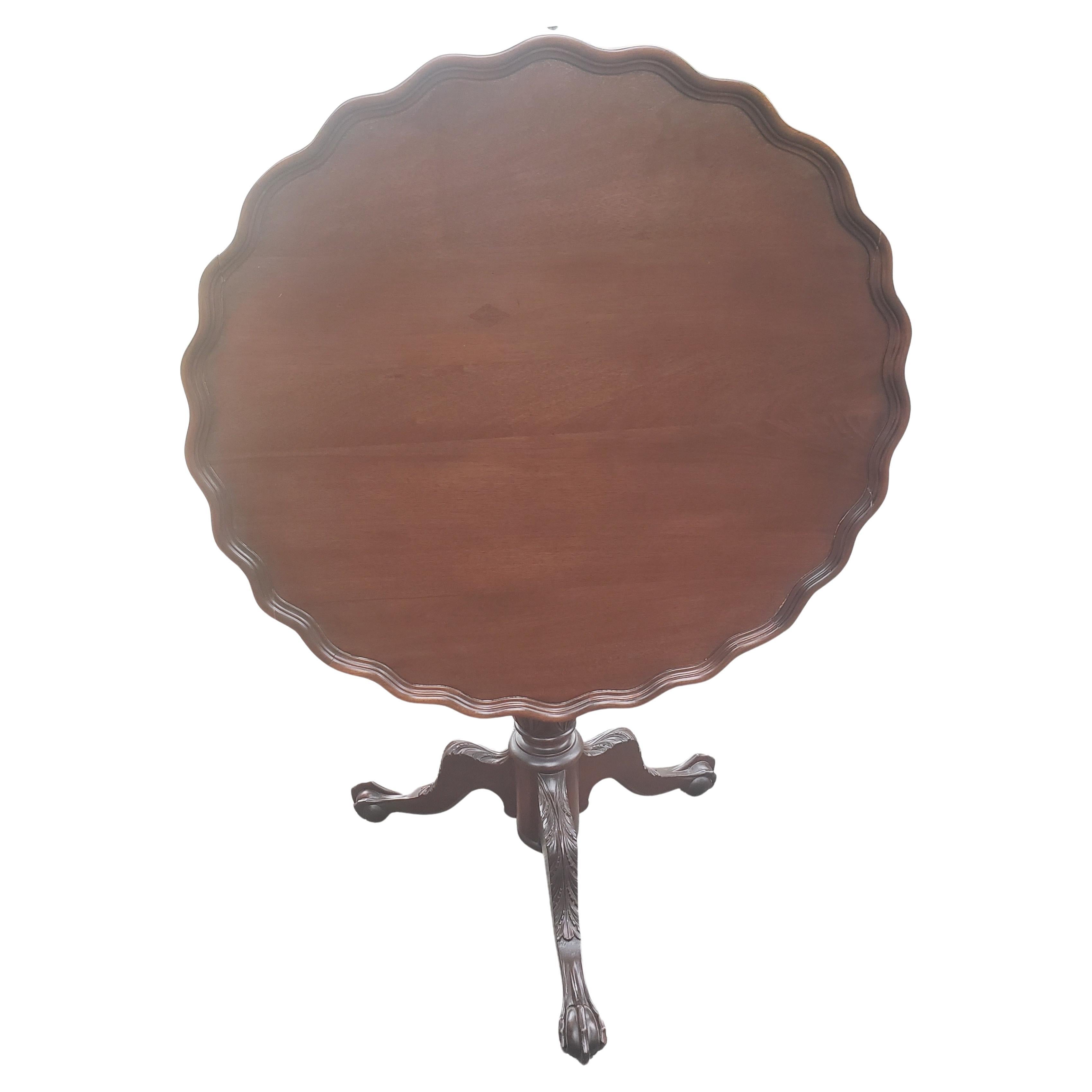 Exquisite antique tilt top pie crust pedestal mahogany tea table / center table in very good vintage condition from the 1930s. Large pie crust top over a hand carved pedestal supported by carved acanthus leaves and terminating with ball and claw